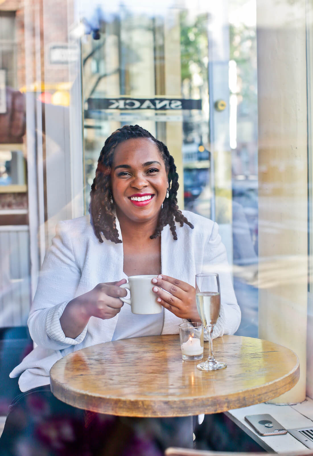 Portrait of Dr. Aprile Andelle, a smiling Black woman with dark braided hair wearing a sleeveless purple top, resting her chin on her hand against a beige background