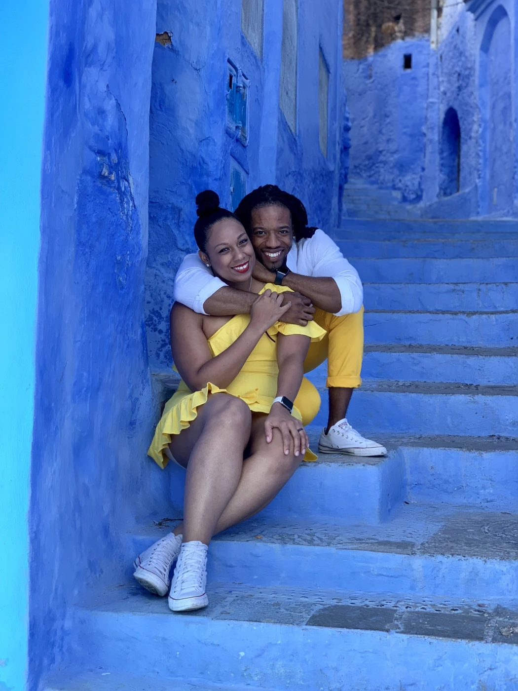 Kes and Jaz embracing and smiling at the camera on blue steps.
