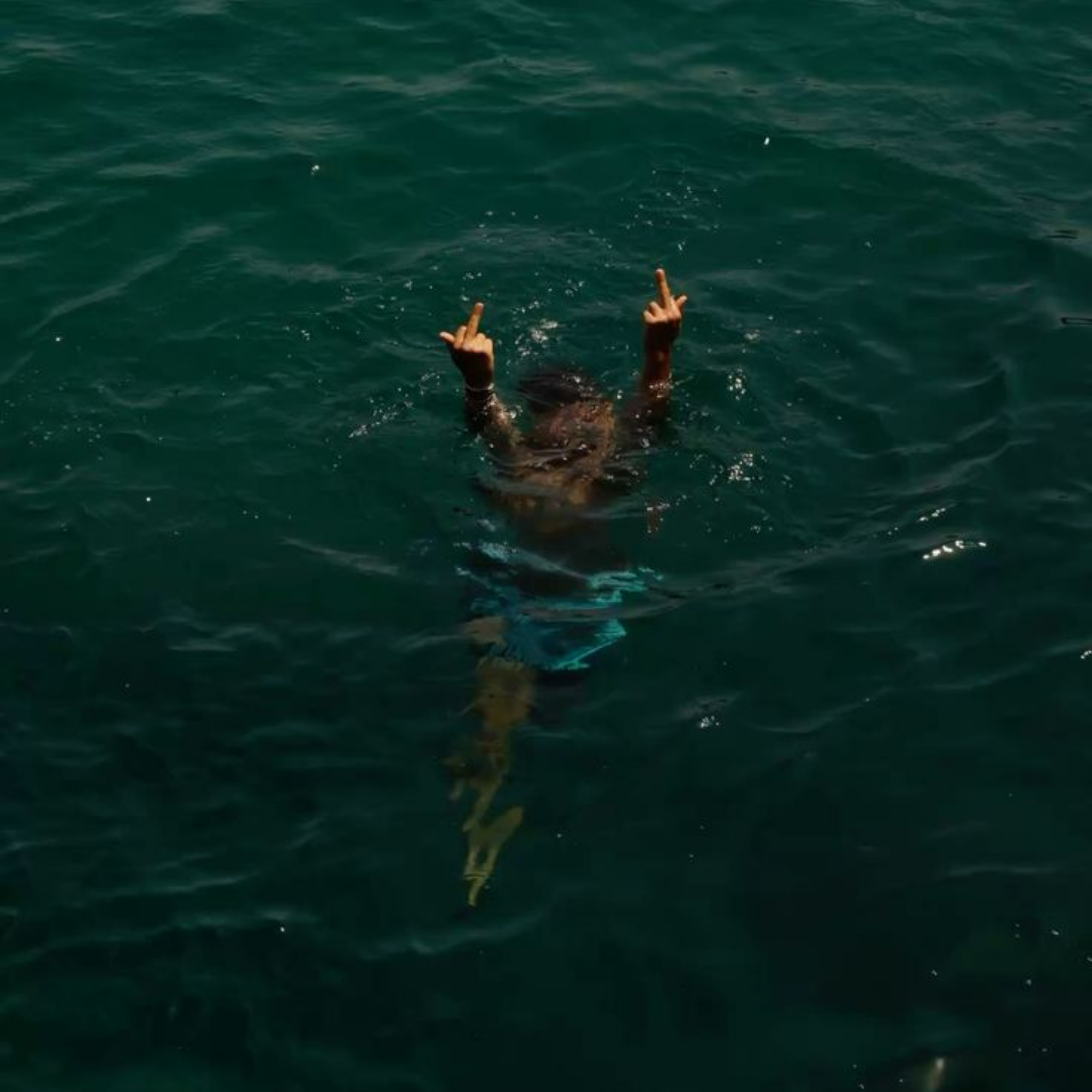 A woman in open water, both hands raised in unapologetic defiance