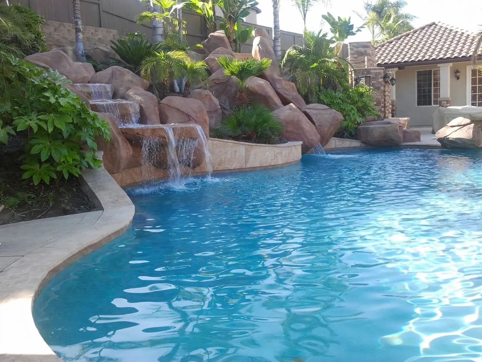 Rock waterfall flowing into a swimming pool with palms behind it