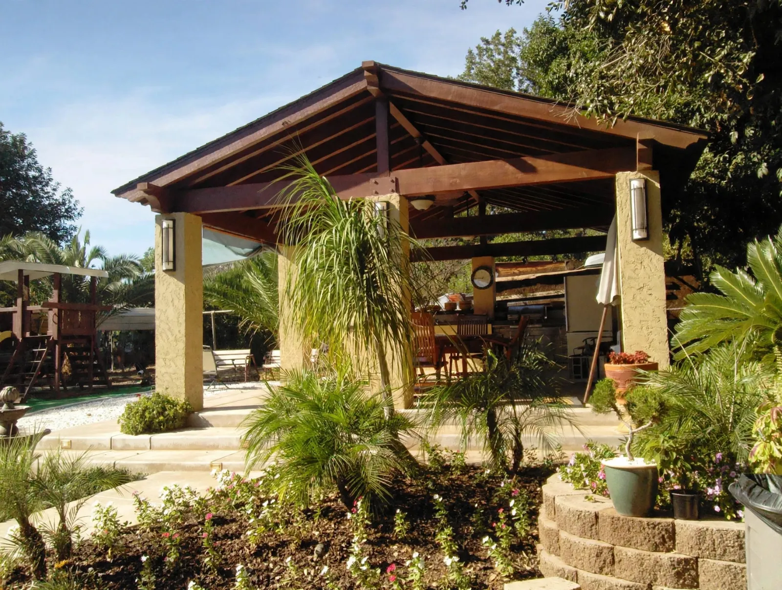 Wood patio cover on stucco columns with a planted yard in front