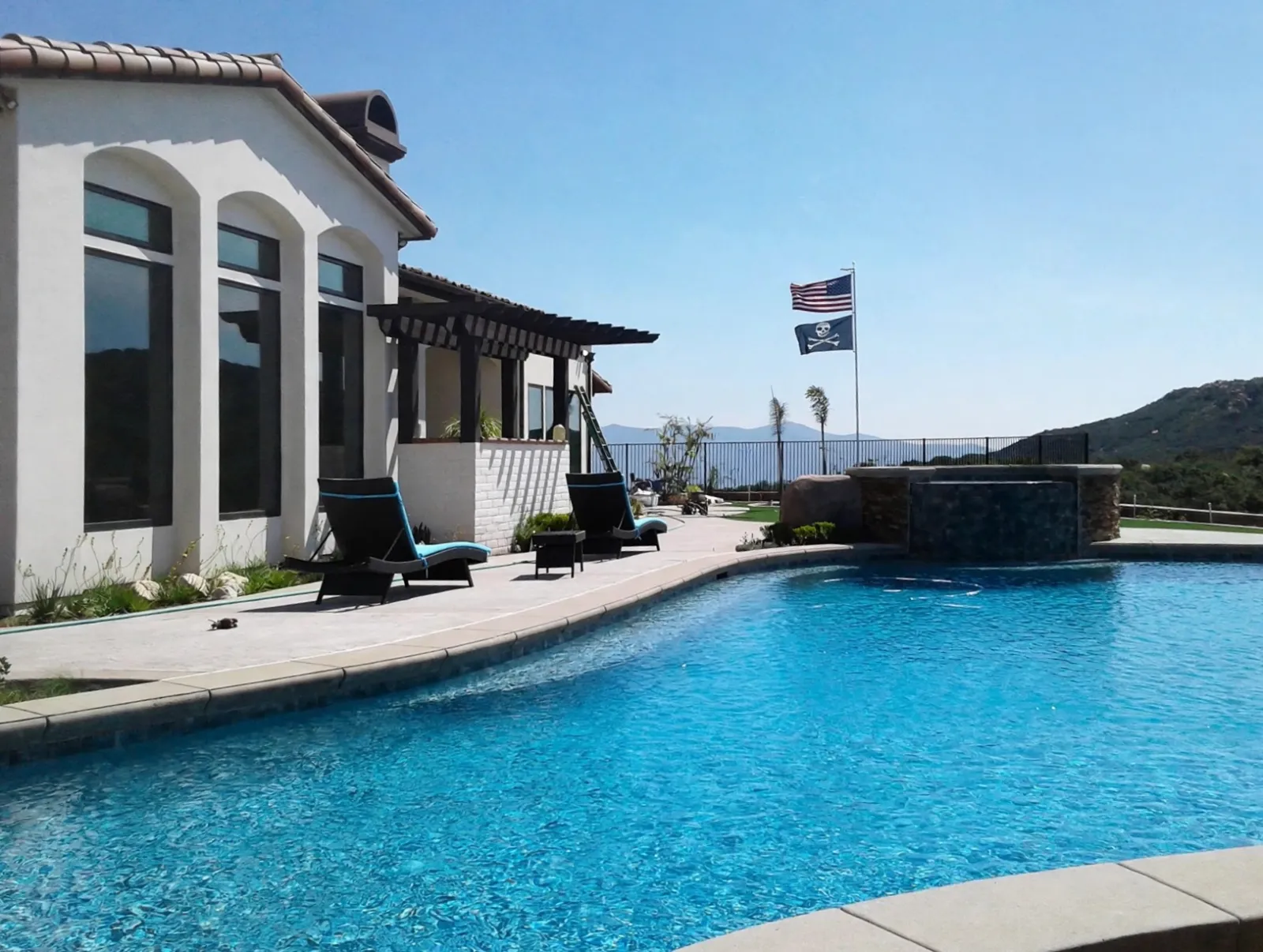 Concrete pool deck and swimming pool beside a hillside home