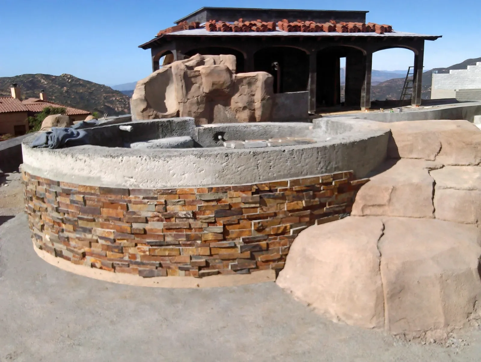 Round raised spa faced in stacked stone with faux boulders beside it