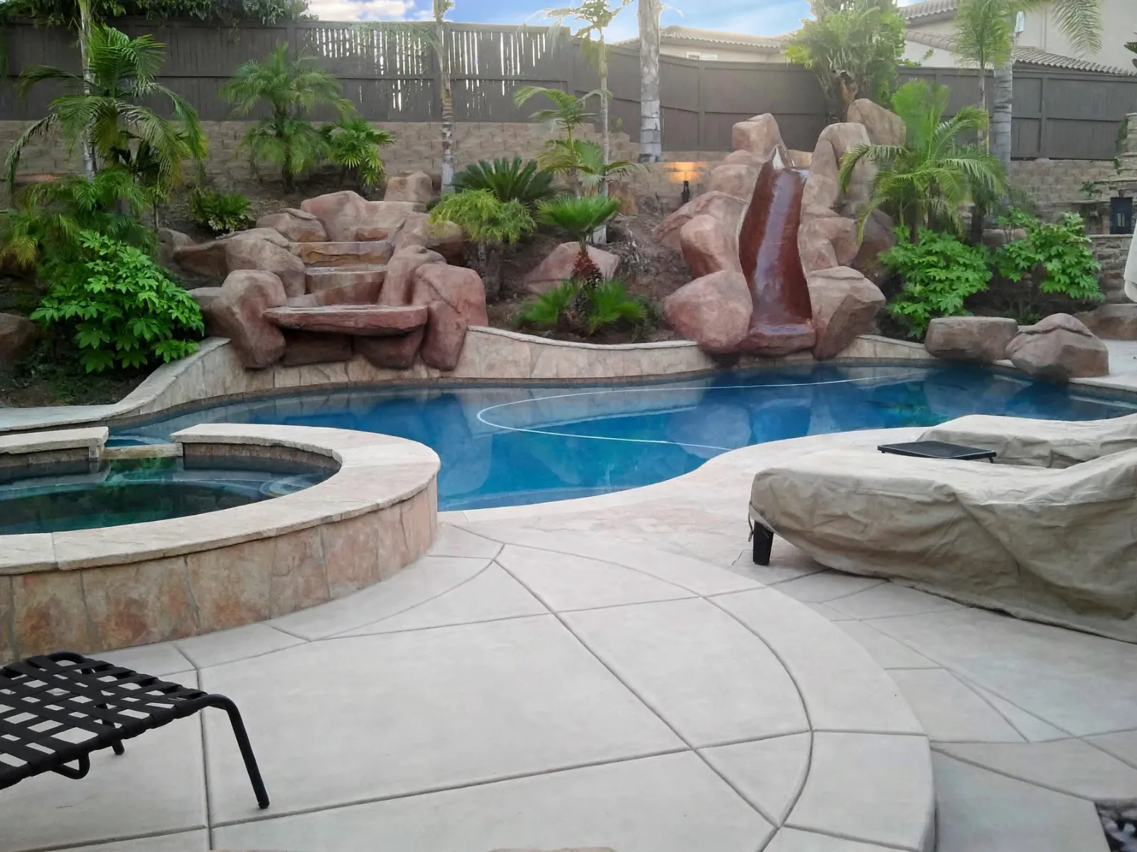 Saw-cut concrete pool deck around a raised spa with a rock waterfall behind