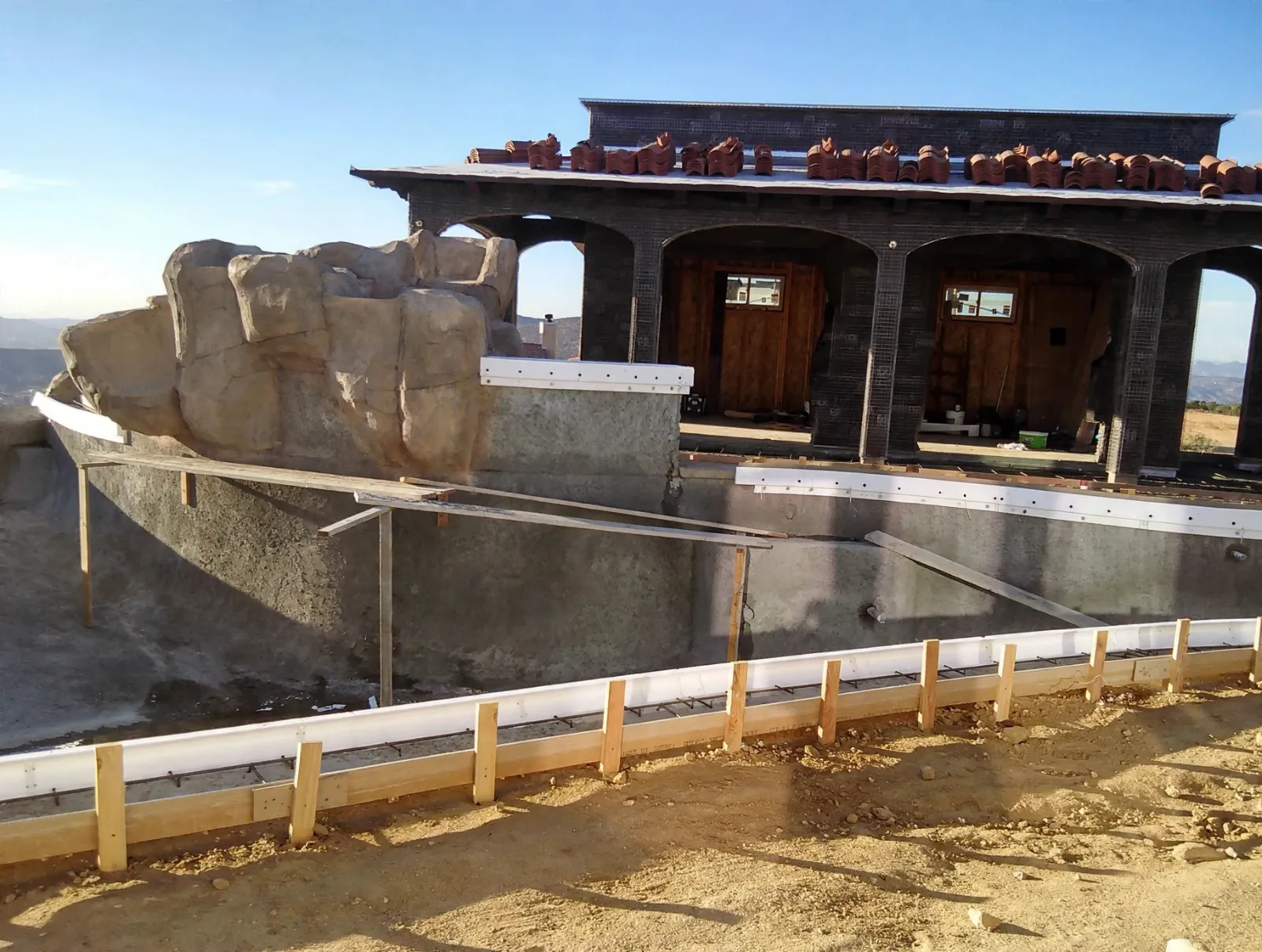Pool shell and faux rock grotto under construction below an outdoor room
