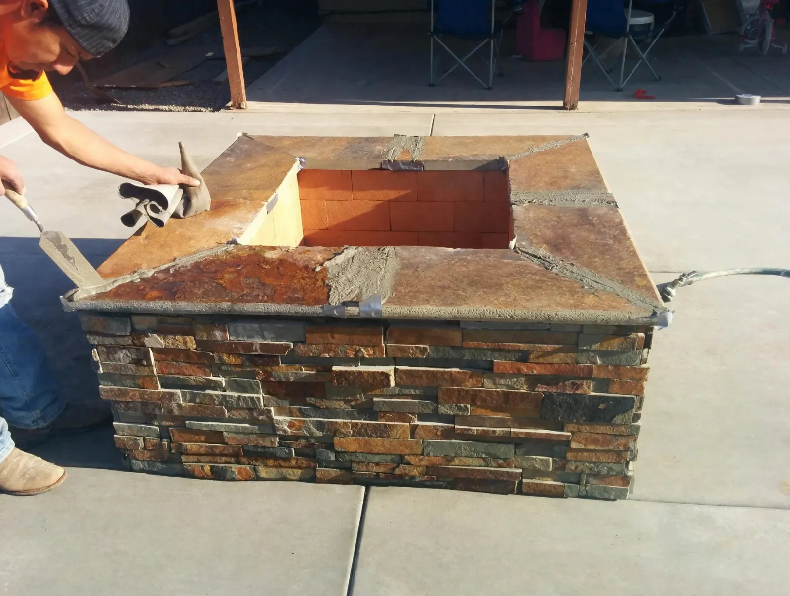 Square fire pit faced in stacked stone on a concrete patio