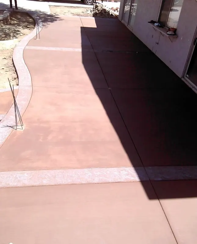 Colored concrete walkway with stamped bands along a house