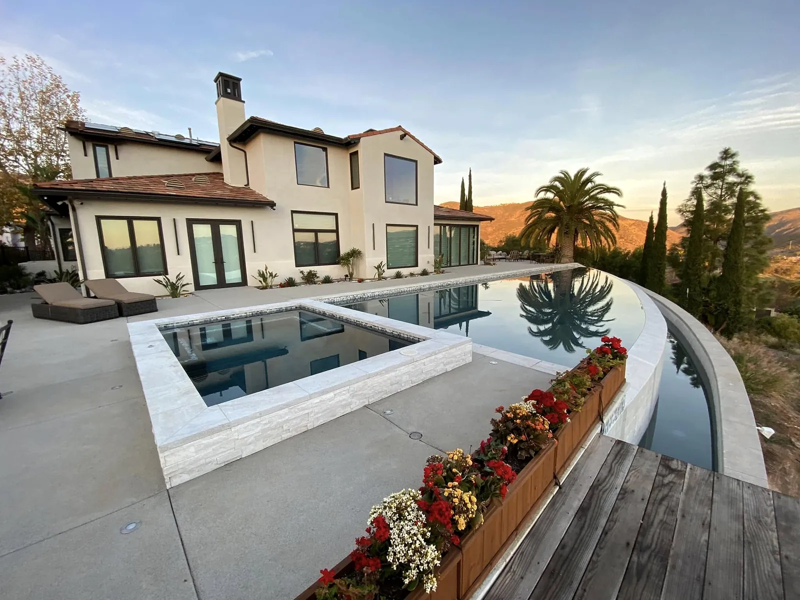 Concrete pool deck around a raised spa and an infinity-edge pool at sunset