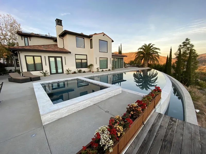 Concrete pool deck around a raised spa and an infinity-edge pool at sunset