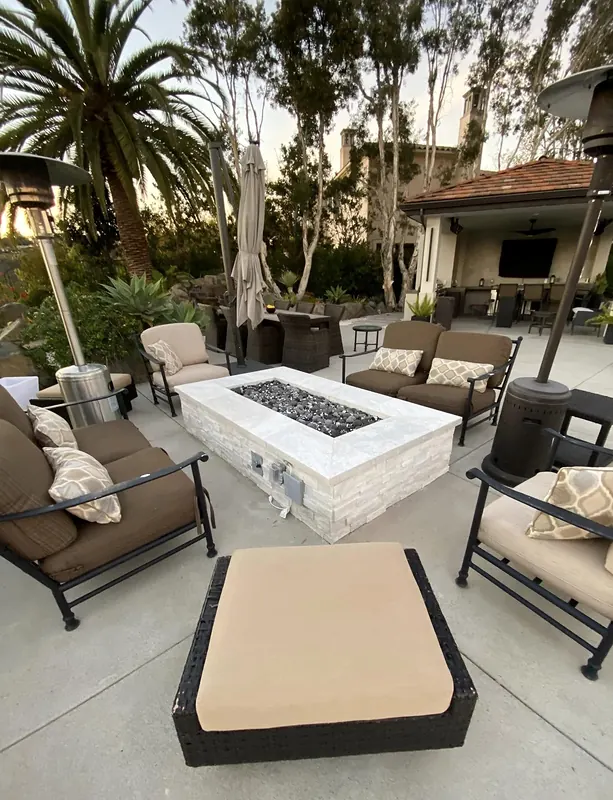 Stacked-stone fire pit and seating on a concrete patio with a pavilion beyond