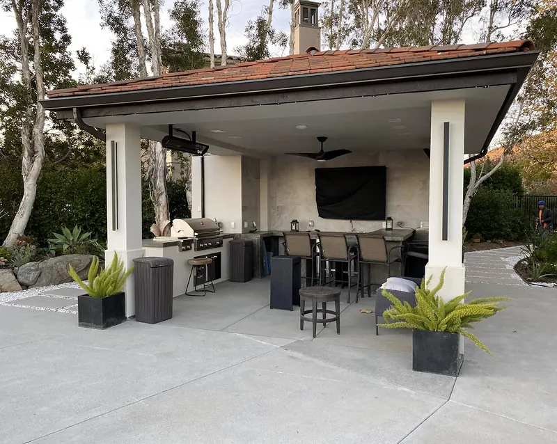 Tile-roof outdoor kitchen pavilion with bar seating on a concrete patio