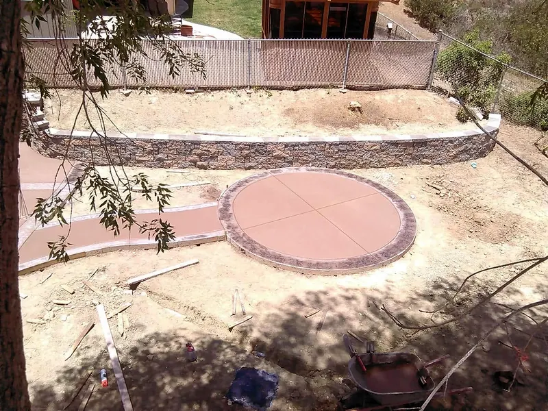 Round colored concrete patio below a block retaining wall