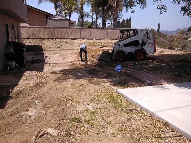 Skid steer grading a yard beside a new concrete pad
