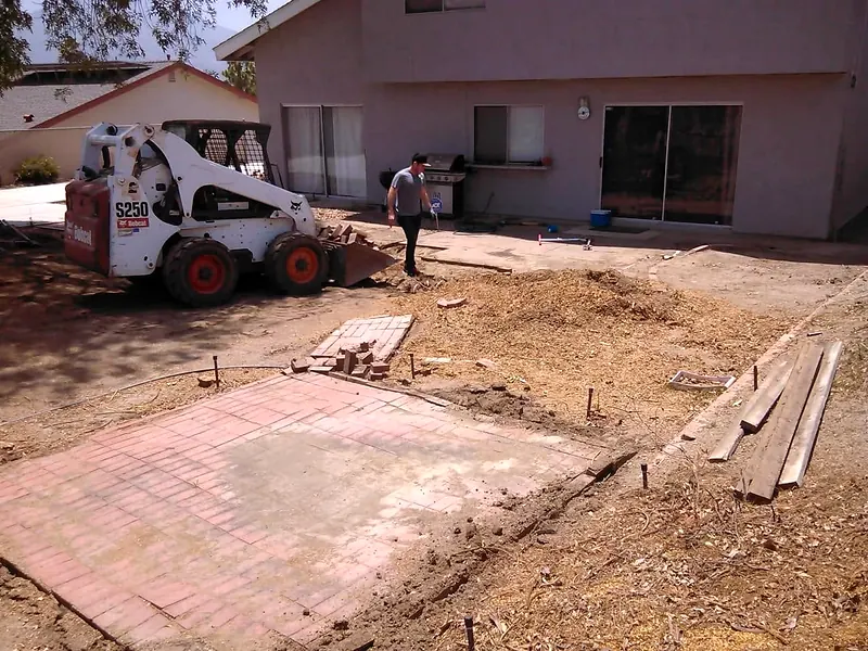 Skid steer clearing a yard next to old brick paving