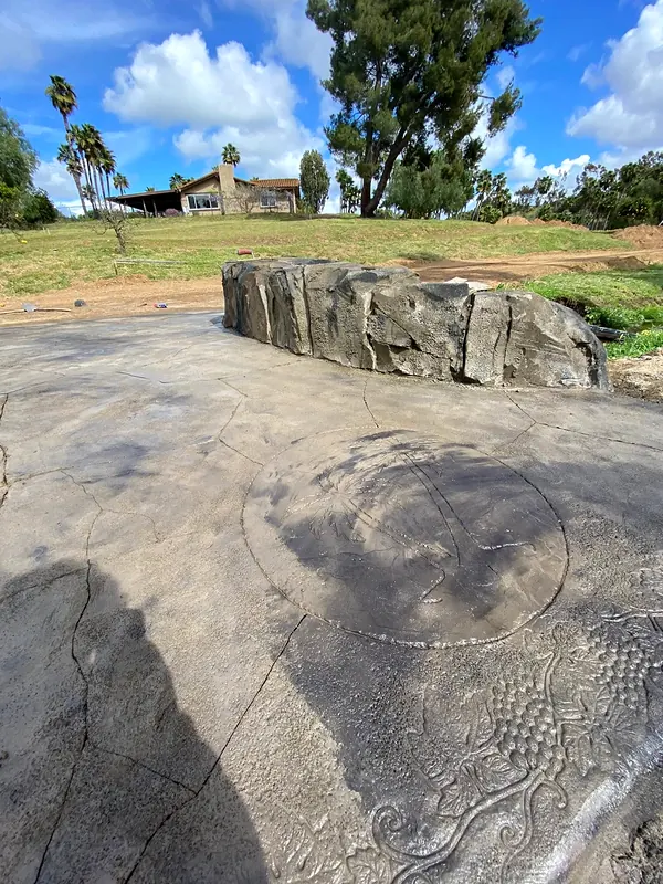 Stamped concrete with a carved medallion beside a faux rock seat wall
