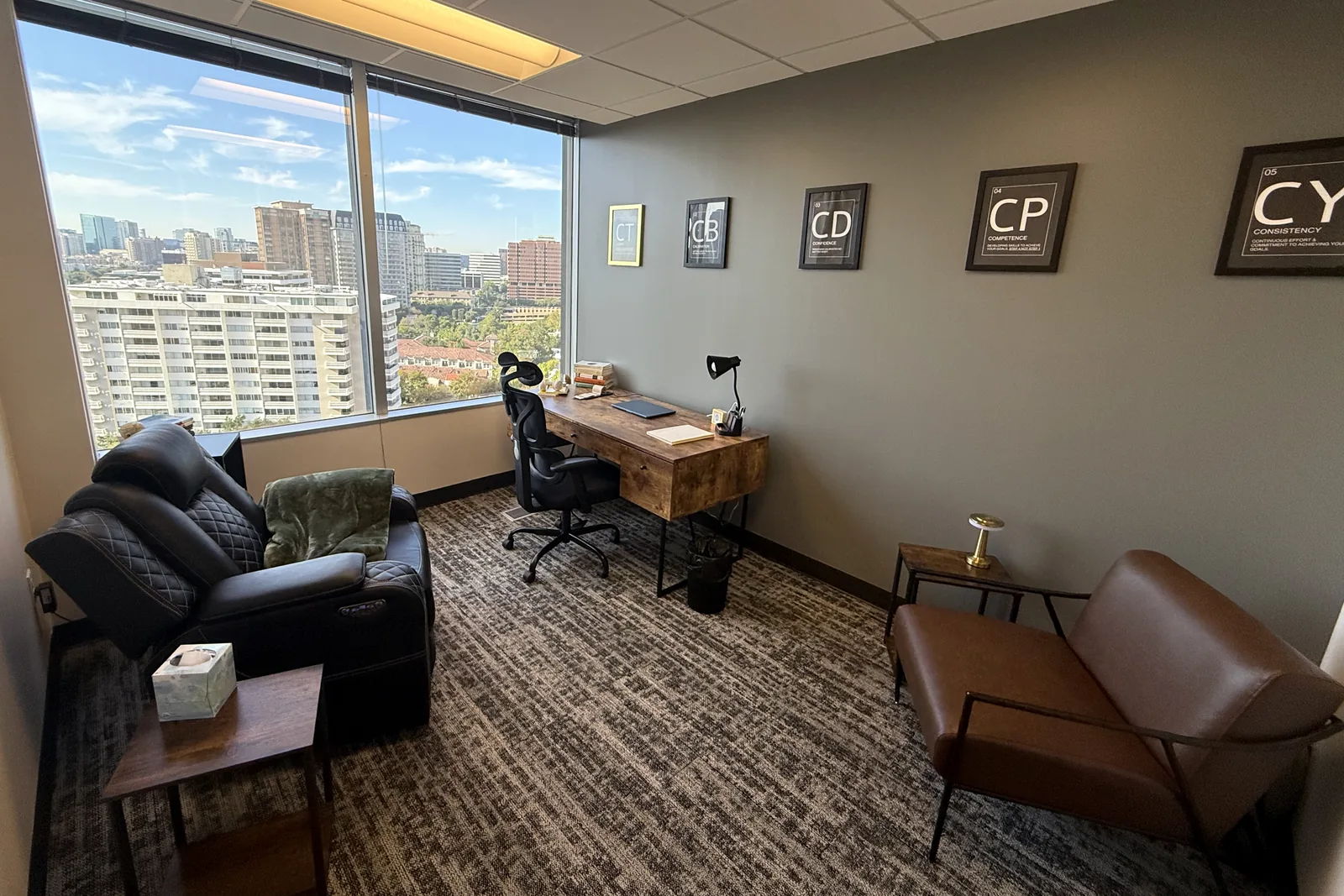 Identity 2.0 Hypnotherapy office in Dallas: hypnotherapy recliner, desk and framed Identity 2.0 dimension posters, with floor-to-ceiling windows over the Oak Lawn skyline