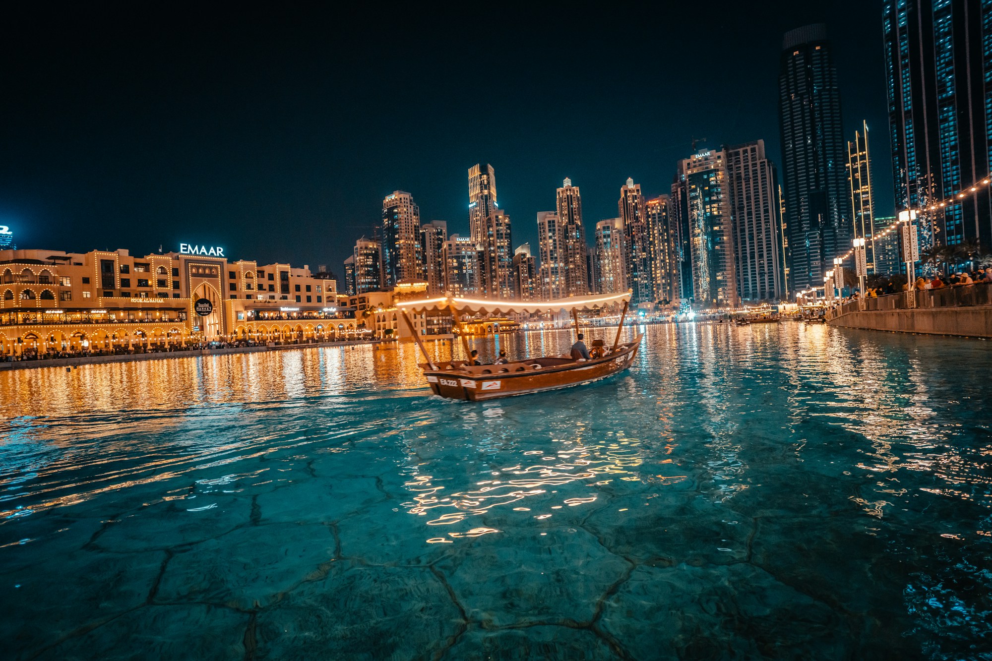 A traditional wooden dhow strung with lights on the water in Dubai at night