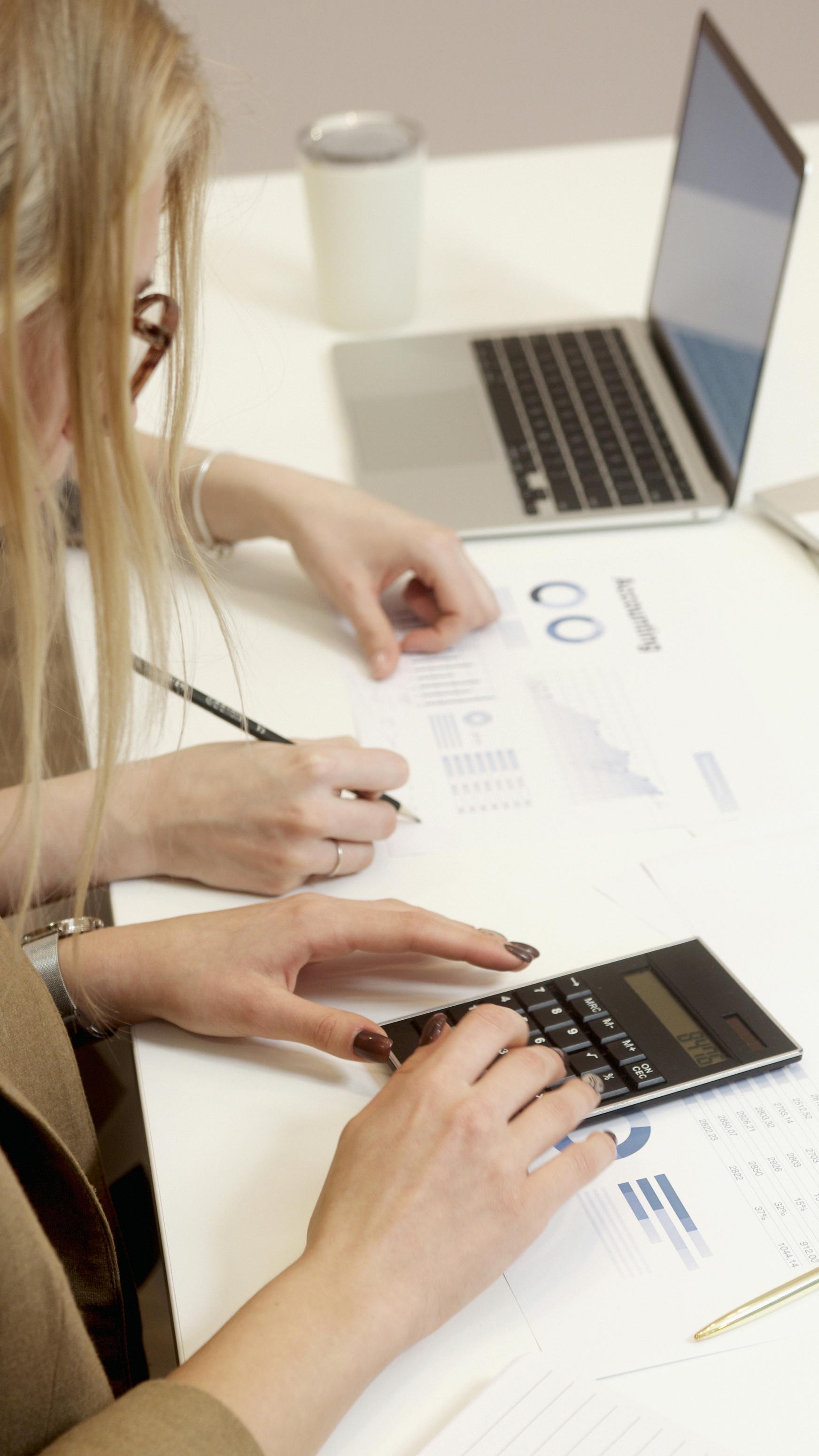 A professional reviewing printed analytics documents and using a calculator at a white desk, representing the commercial cost of unstructured social media management. A professional reviewing printed analytics documents and using a calculator at a white desk, representing the commercial cost of unstructured social media management.