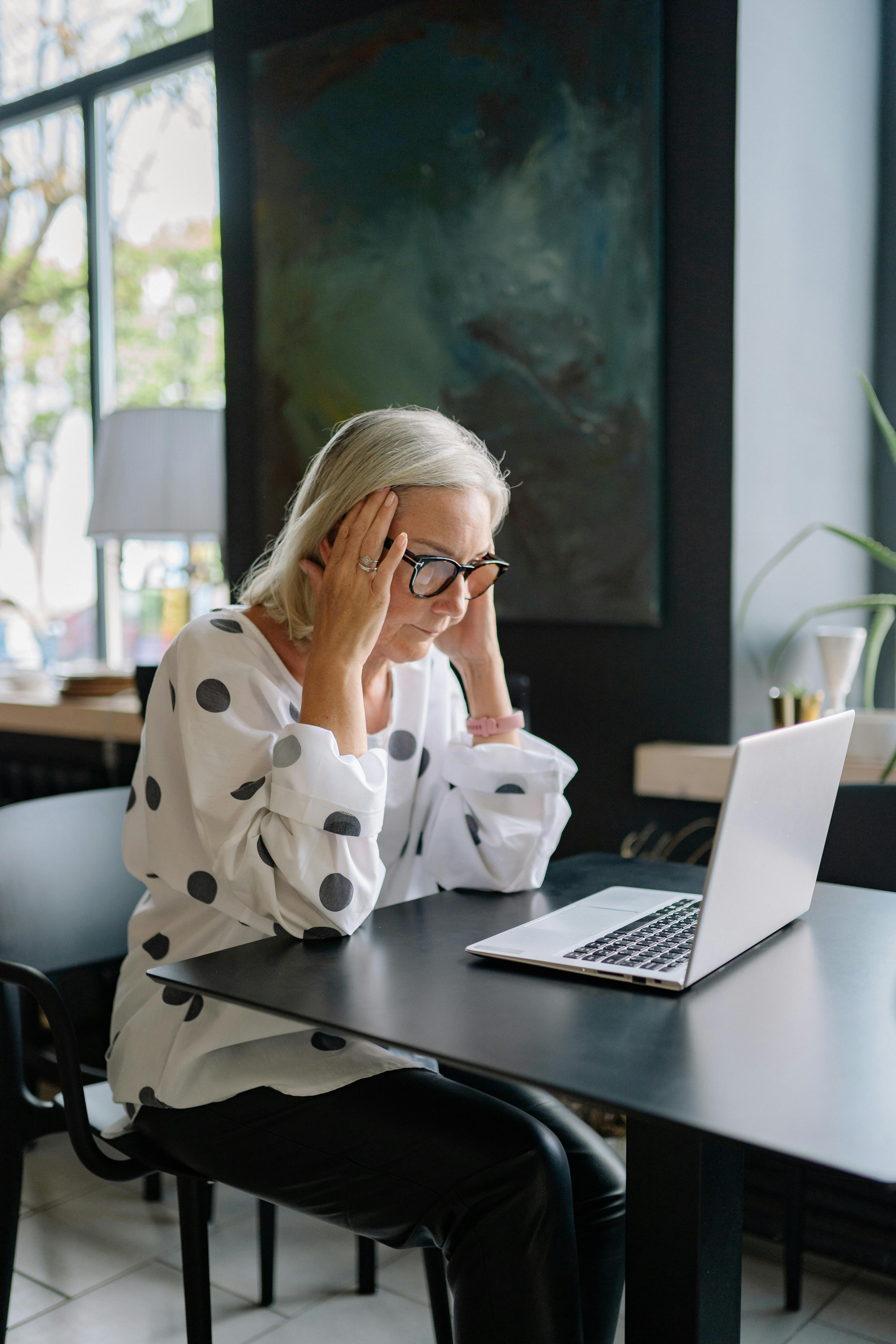 A business owner at her laptop showing the strain of manually managing every part of her business without an automated marketing system in place A business owner at her laptop showing the strain of manually managing every part of her business without an automated marketing system in place