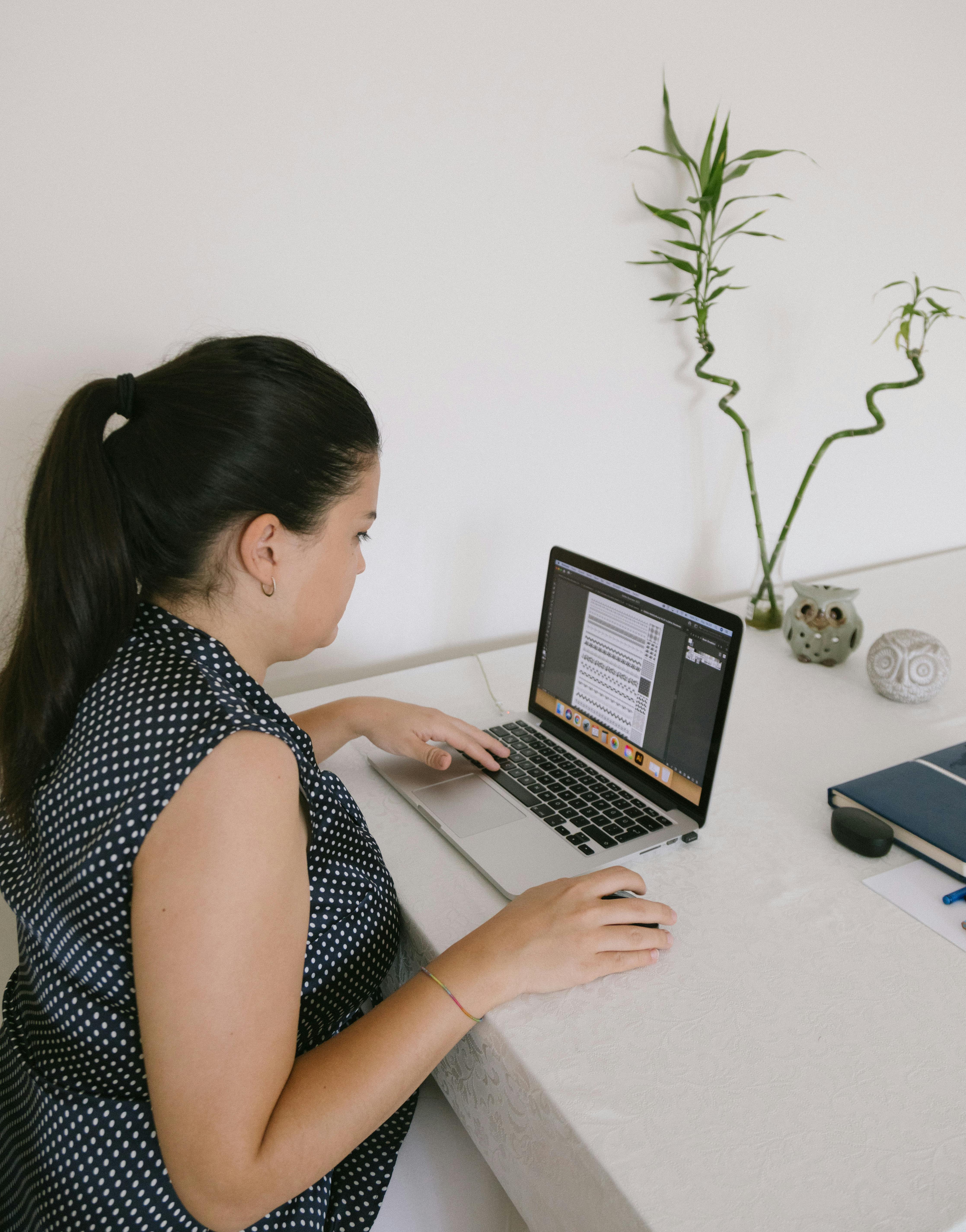 A woman writing in a notebook alongside a laptop reviewing her work at a wooden desk with a phone visible. A woman writing in a notebook alongside a laptop reviewing her work at a wooden desk with a phone visible.