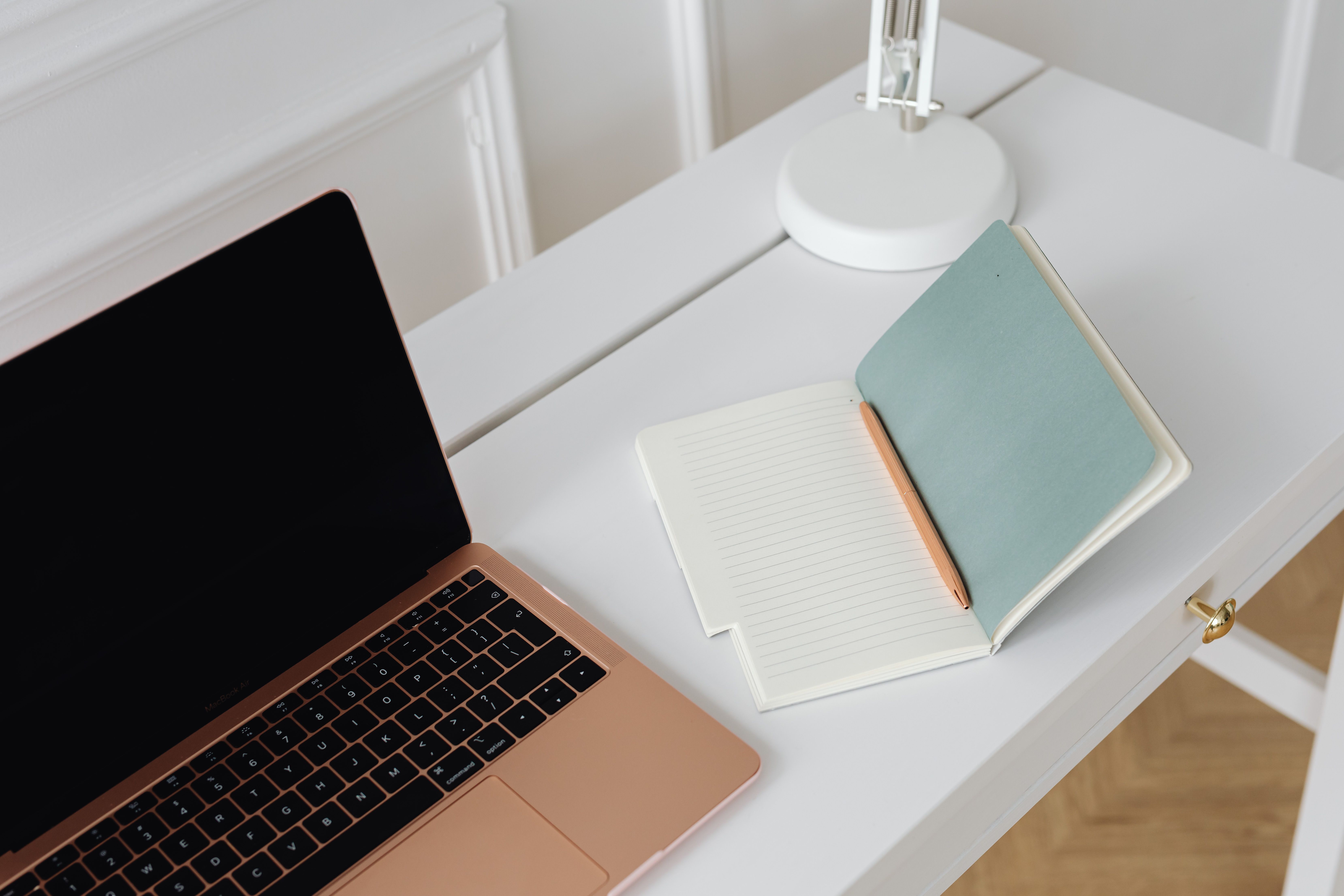 A gold laptop and open notebooks on a clean white desk representing intentional social media content planning for established UK service providers. A gold laptop and open notebooks on a clean white desk representing intentional social media content planning for established UK service providers.