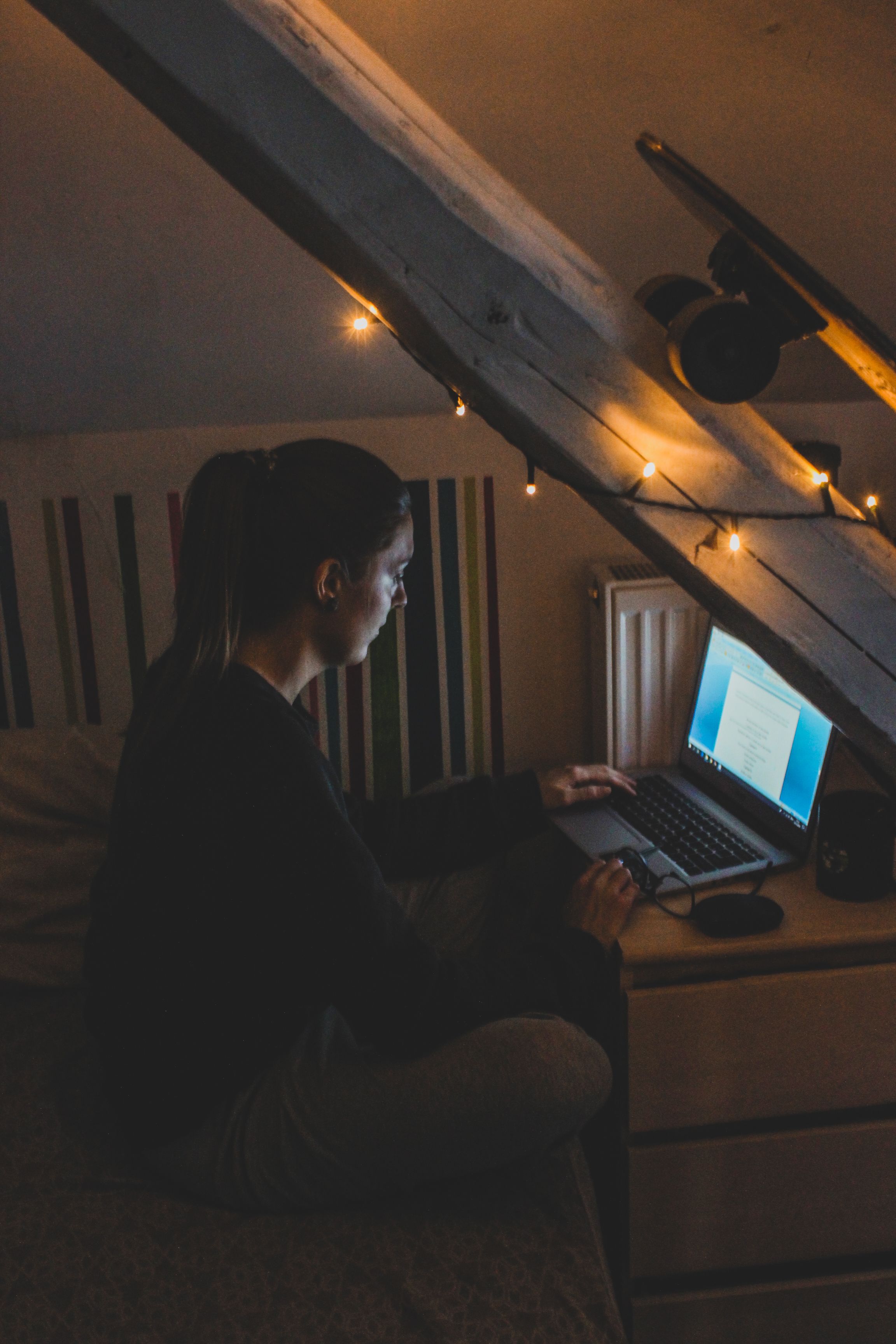 A woman working alone late at night on a laptop in a dimly lit room representing the personal and professional cost of doing everything yourself as a small business owner. A woman working alone late at night on a laptop in a dimly lit room representing the personal and professional cost of doing everything yourself as a small business owner.