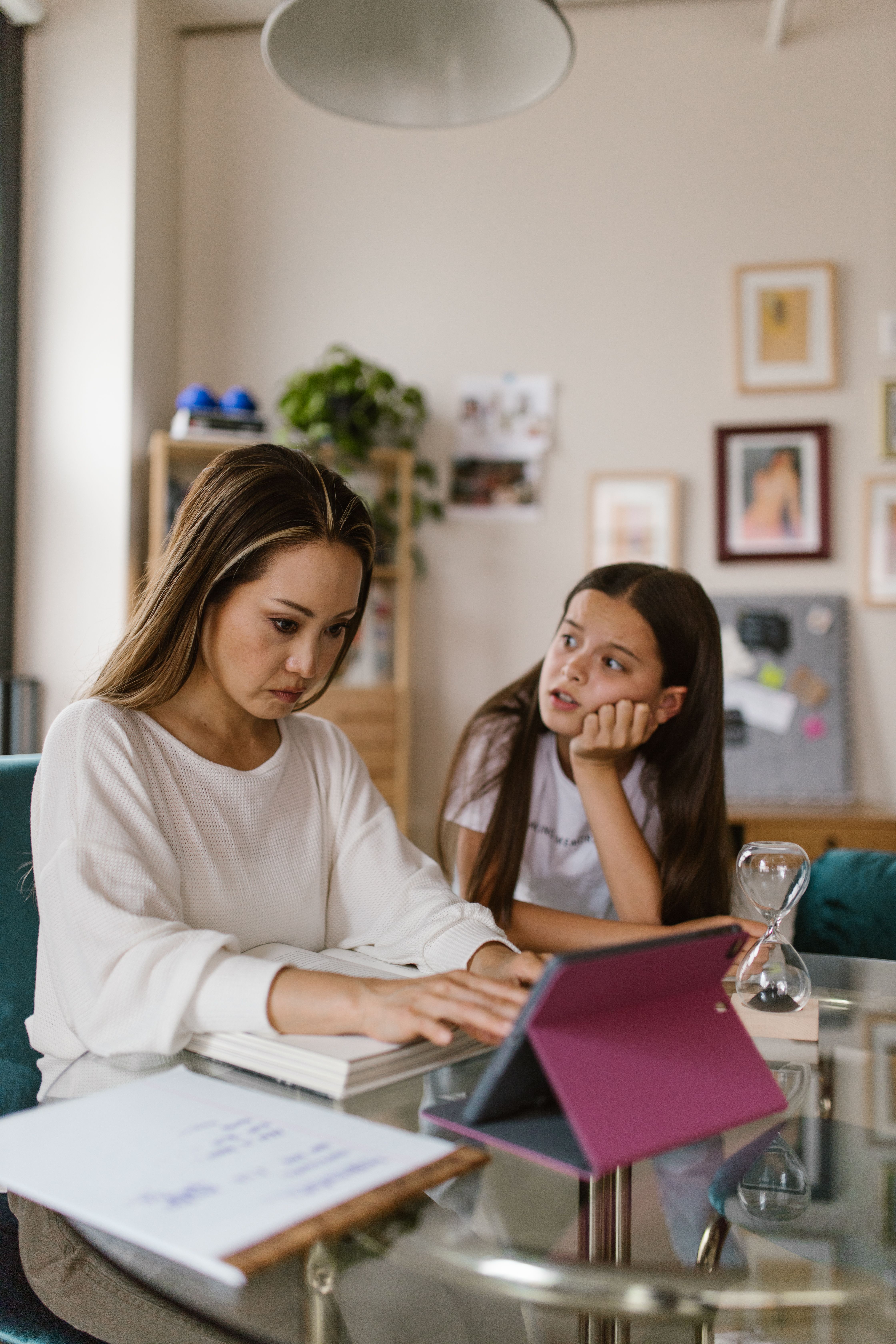A mother working on a device while her daughter sits beside her looking for her attention, representing the personal cost of carrying too much in business on family presence. A mother working on a device while her daughter sits beside her looking for her attention, representing the personal cost of carrying too much in business on family presence.