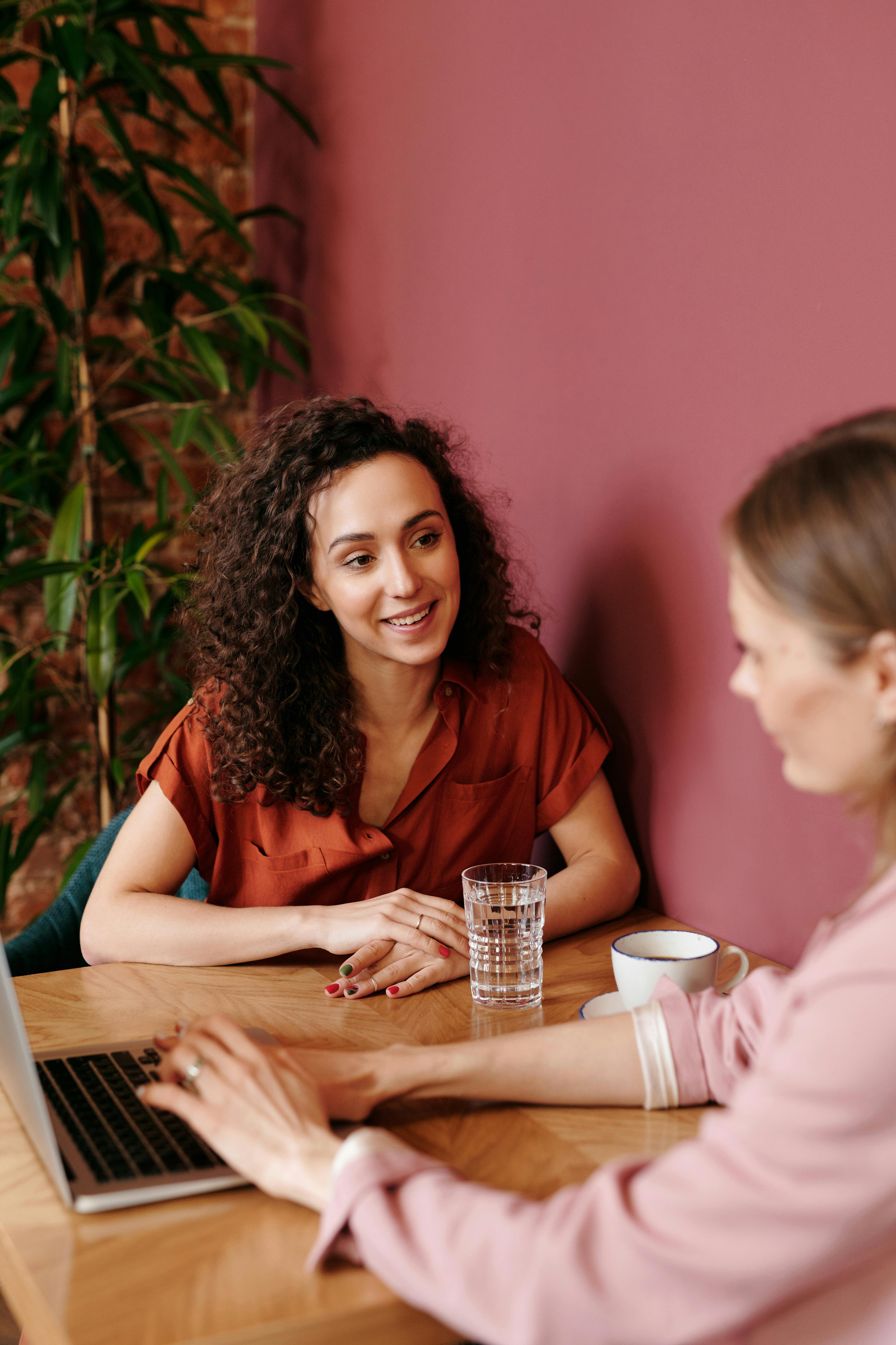 Two women in a focused working conversation across a table representing the strategic partnership that becomes possible when the right support is in place for an established service provider. Two women in a focused working conversation across a table representing the strategic partnership that becomes possible when the right support is in place for an established service provider.