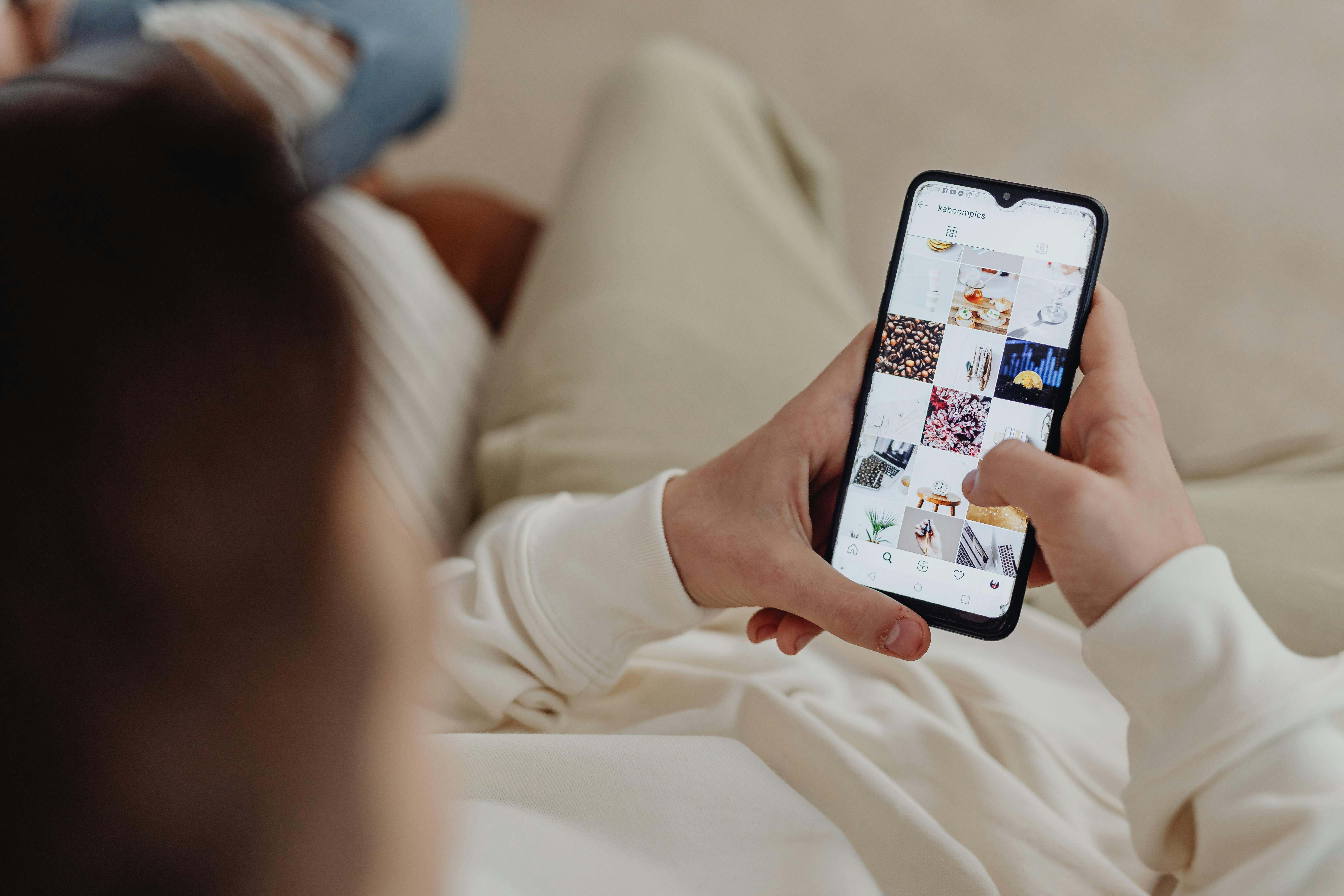 A person relaxing on a sofa scrolling through social media content on their phone in the evening. A person relaxing on a sofa scrolling through social media content on their phone in the evening.