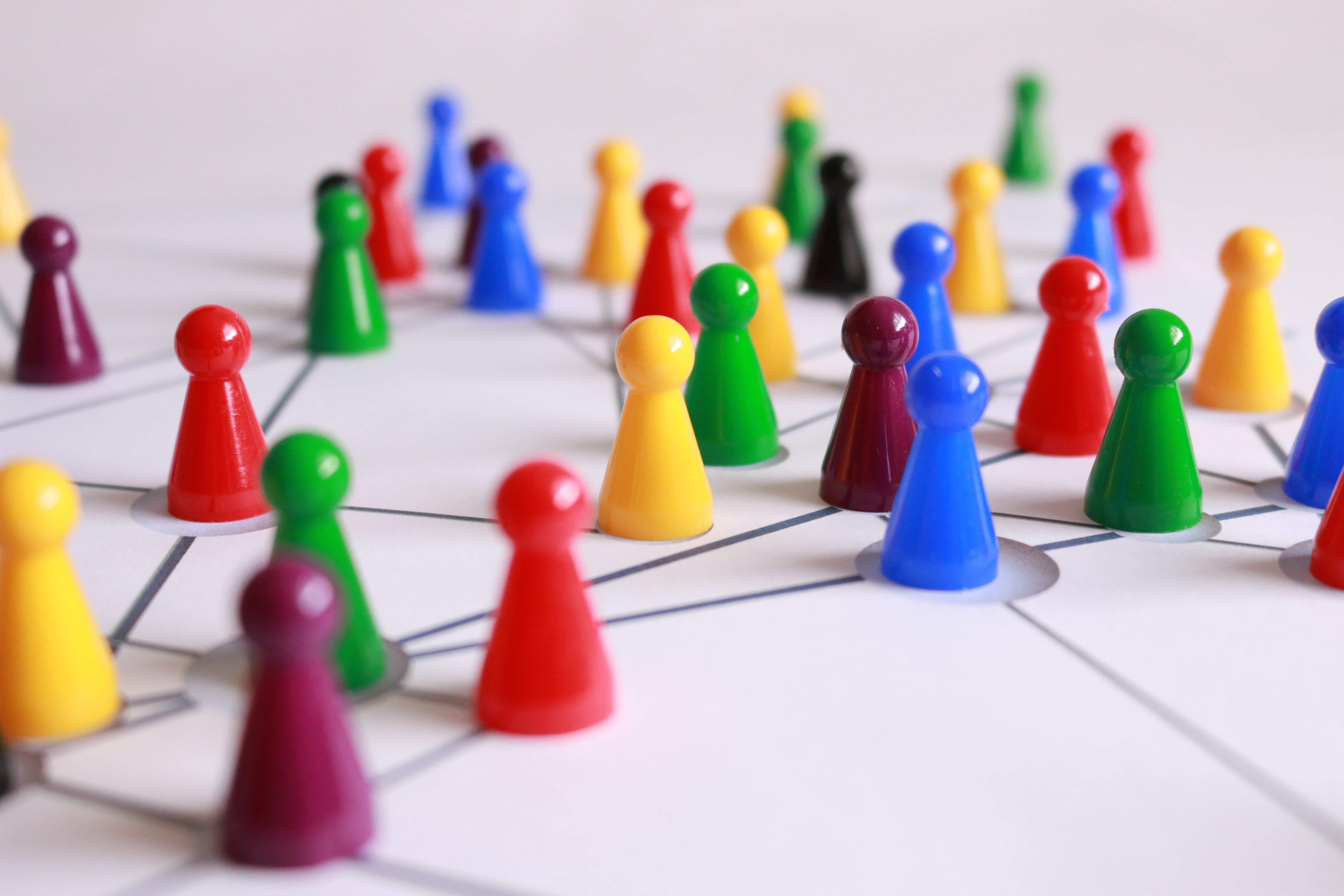Coloured game pieces connected by lines on a white surface representing the multiple connected pathways of a business ecosystem.