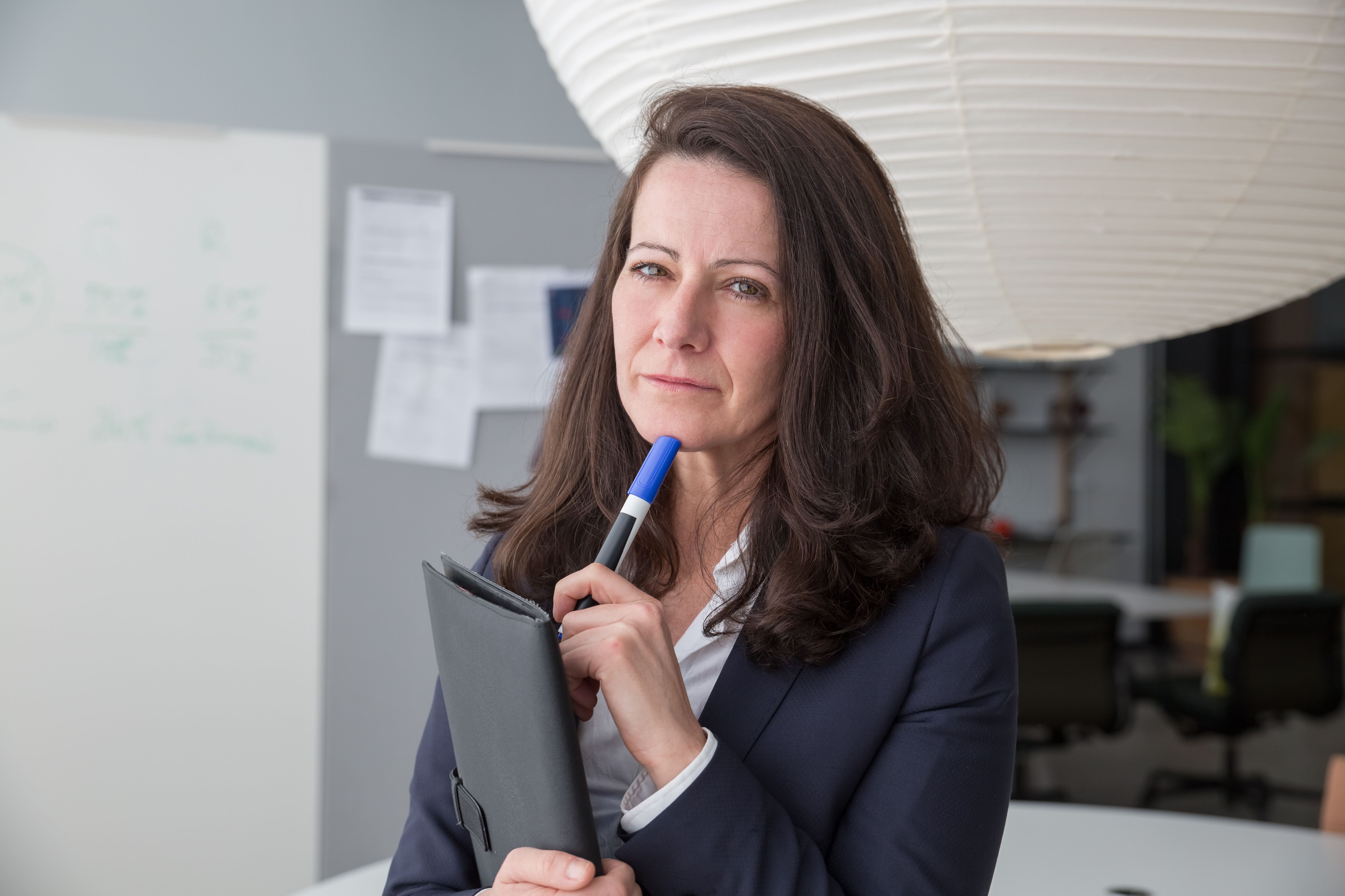 An experienced business strategist holding a clipboard and pen looking thoughtful and considered in a professional environment.