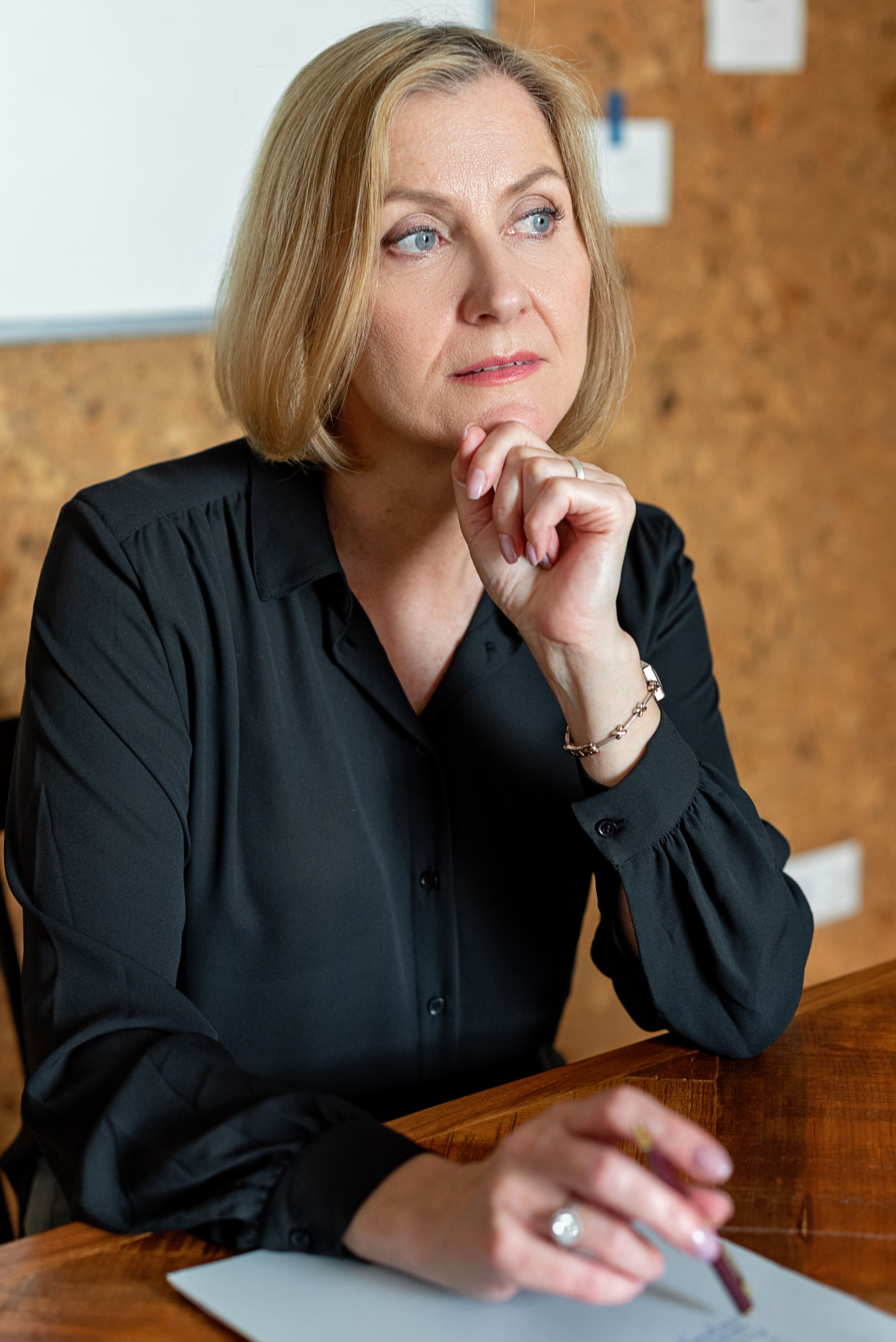 An established business owner sitting at a desk looking thoughtfully upward, hands clasped, considering whether her business is working as well as she believes.