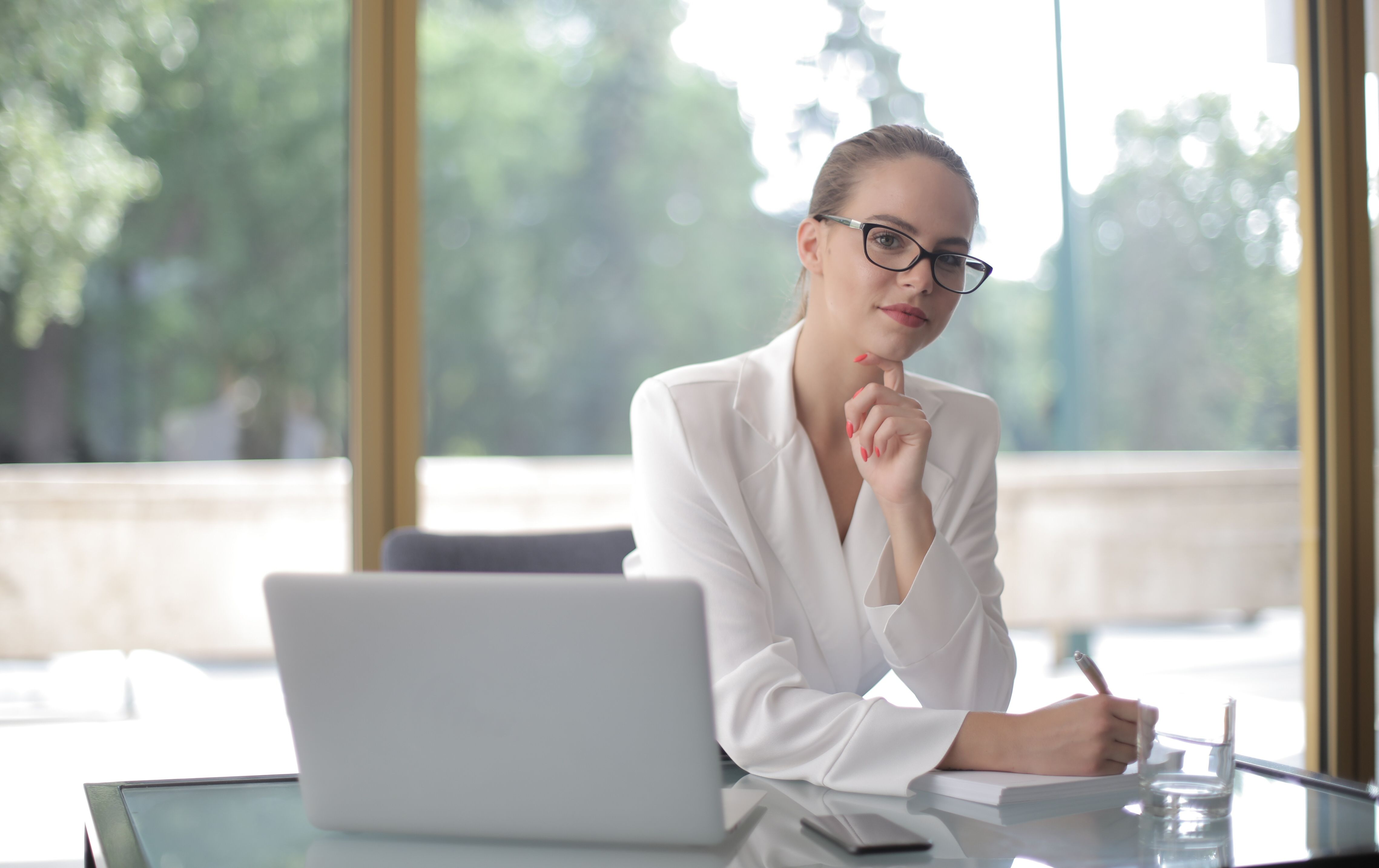 A business owner sitting at a bright desk with a laptop looking forward with a calm and considered expression, ready to take the next step.