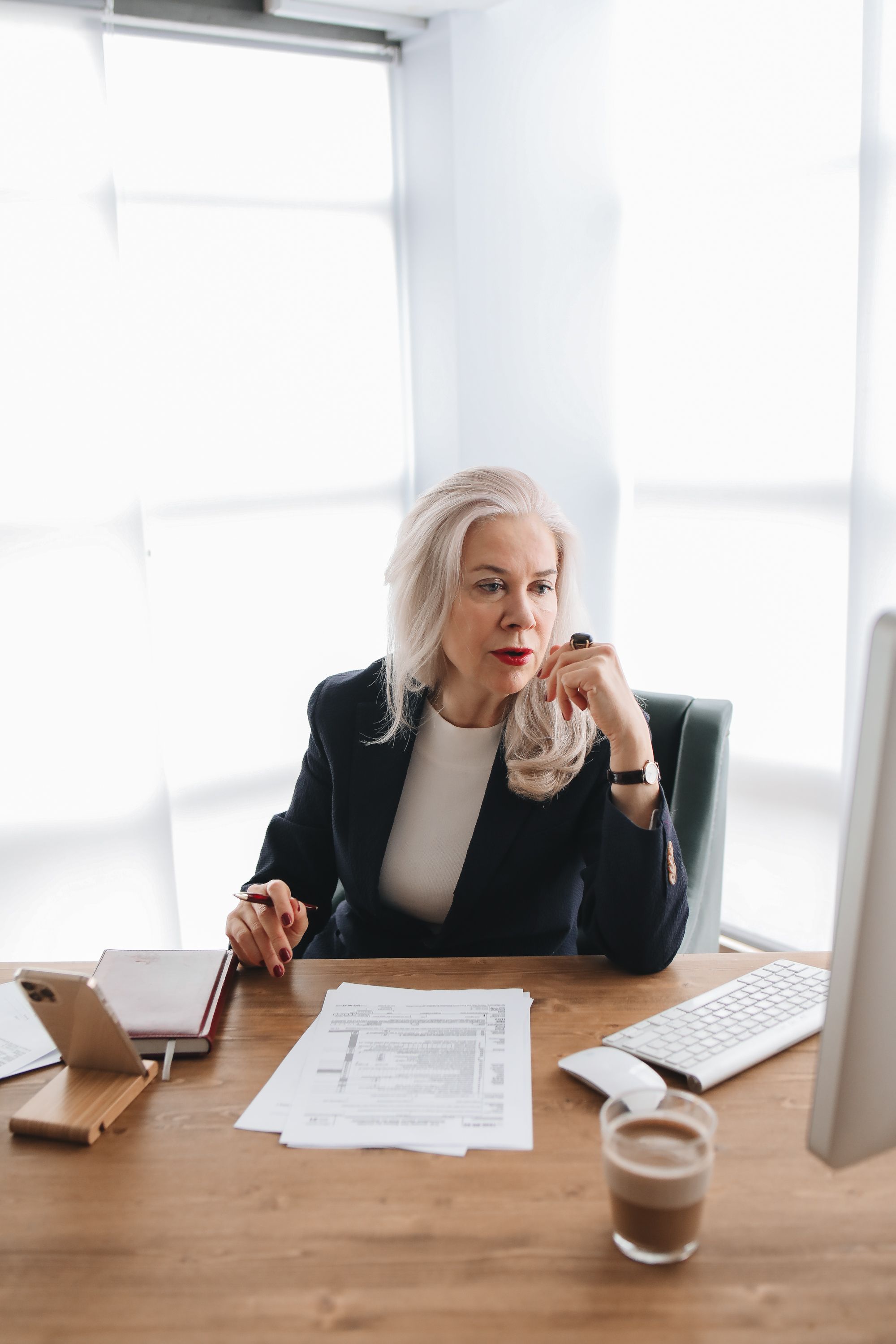 An established business owner sitting at her desk reviewing documents, representing the quiet uncertainty of making marketing decisions without clear evidence of what is working.
