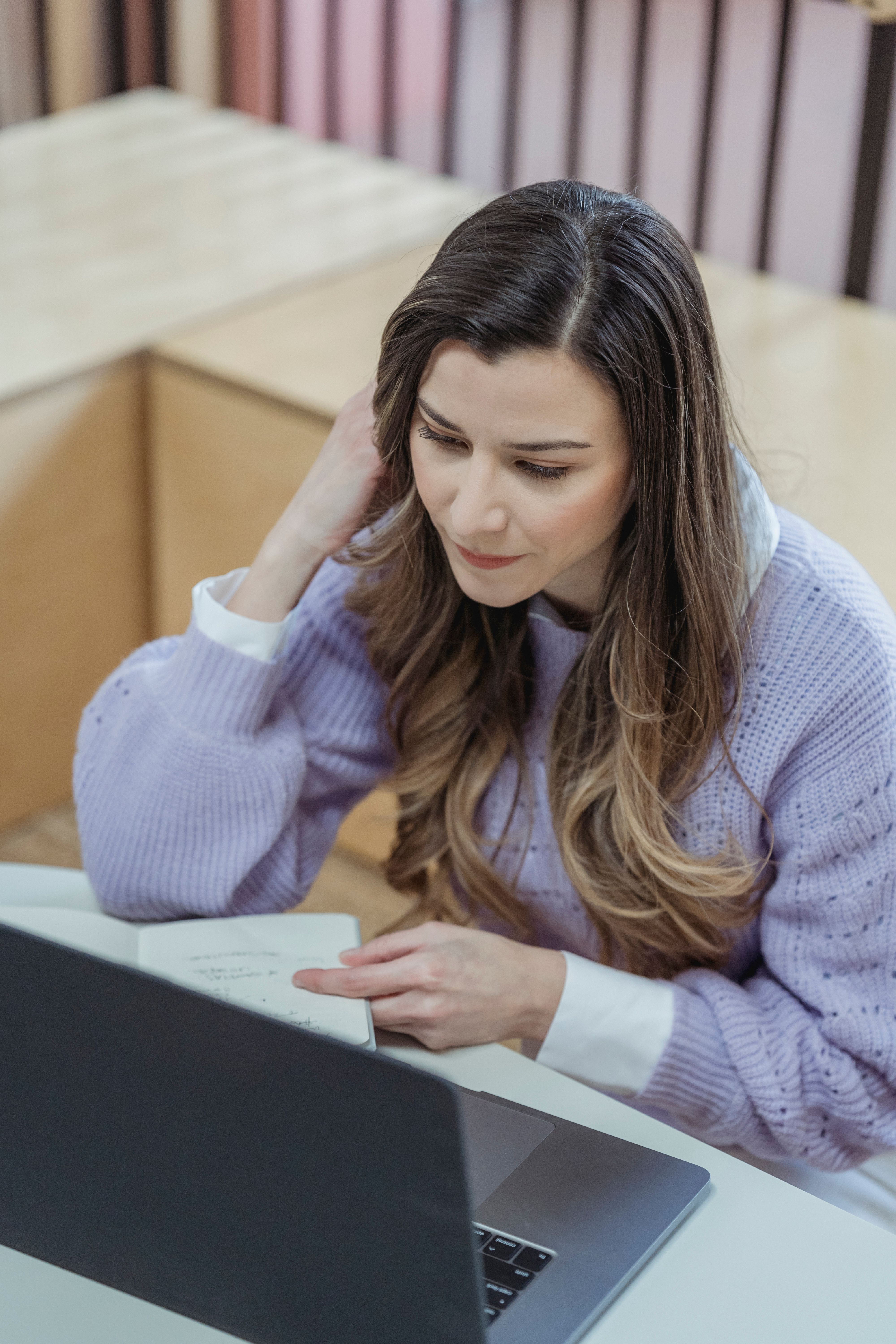 A professional pausing at her laptop with a searching expression, representing the experience of creating brand materials without documented guidelines to work from.