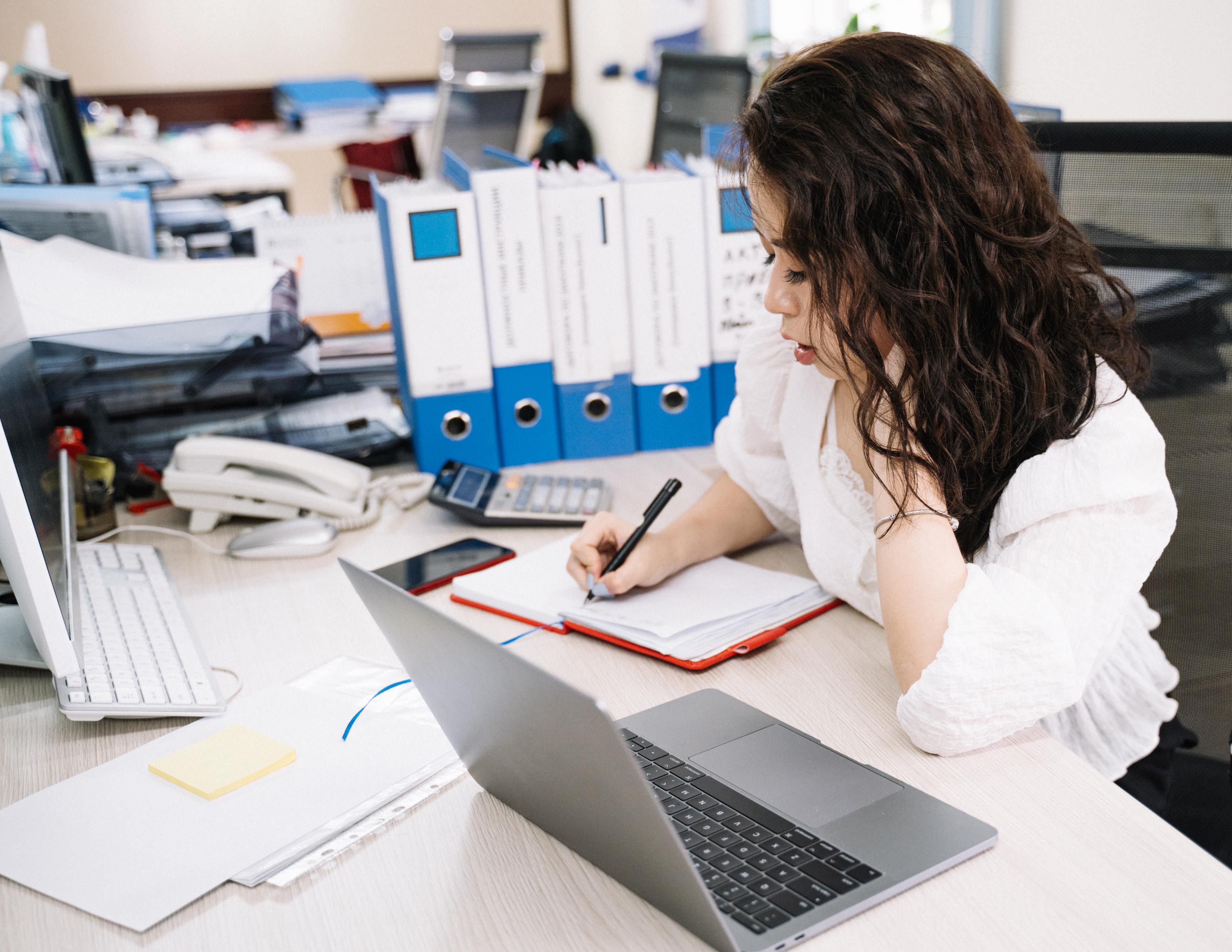 A business owner working at a busy desk surrounded by documents and screens, representing the experience of putting in consistent effort without a strategic direction connecting what goes out to what the business is trying to achieve.