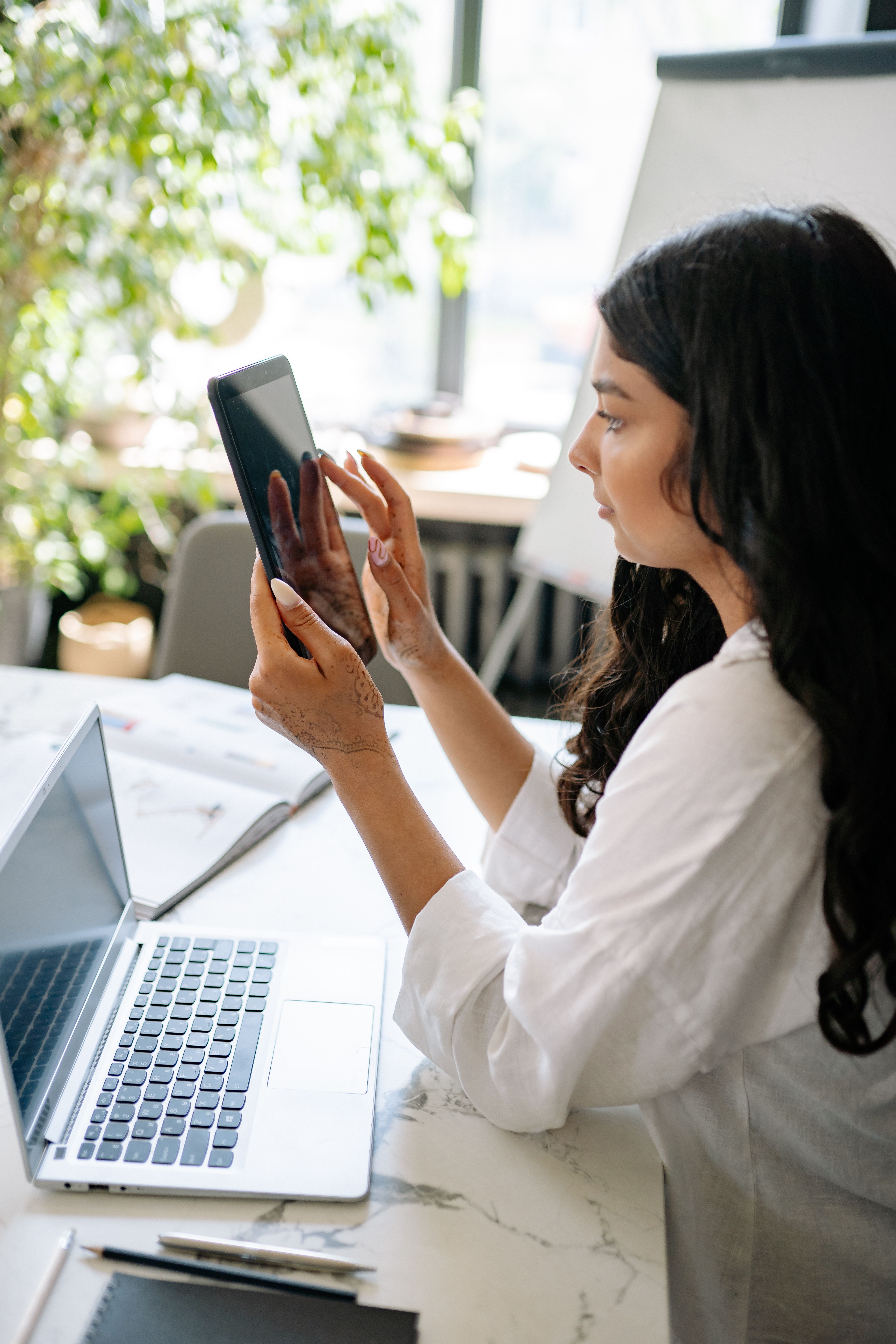 A business owner actively using a digital tablet alongside her laptop, representing the experience of working from a structured digital planning system where everything needed is in one place and ready to use.