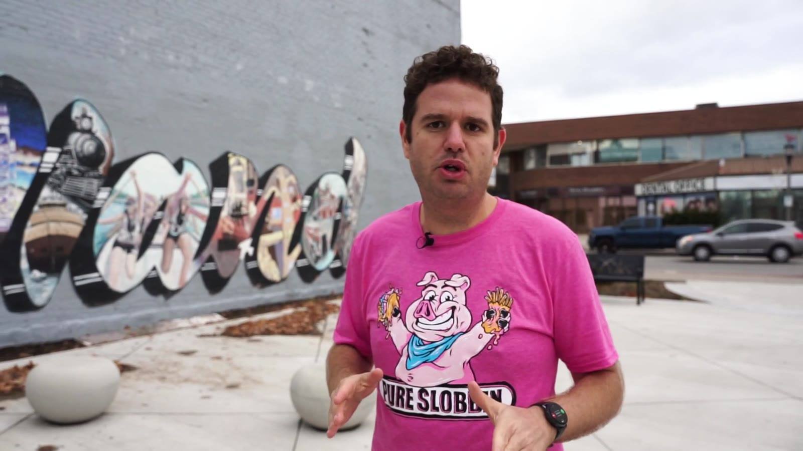 Joe in a pink Pure Slobbin' shirt in front of the Welland mural