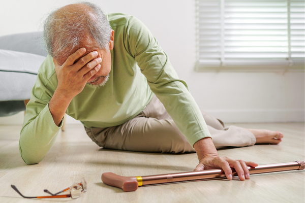 A senior man that has fallen over and laying on the floor holding his head. 