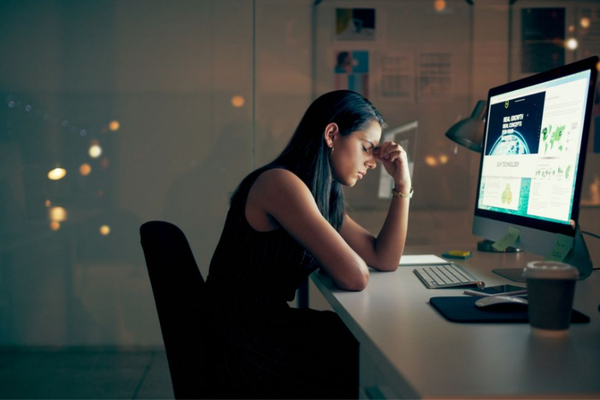 A tired family caregiver holding her head whilst sitting at her work desk.