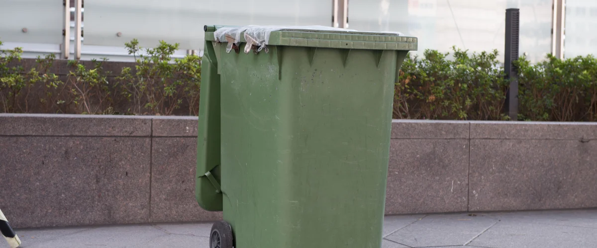 Green outdoor garbage bin placed on sidewalk near building. Green outdoor garbage bin placed on sidewalk near building.