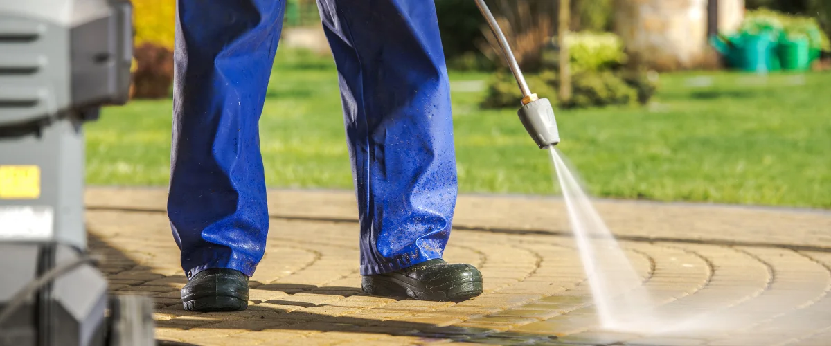 A man in overalls and yellow boots power-washing a patio with a high-pressure washer on a sunny day. A man in overalls and yellow boots power-washing a patio with a high-pressure washer on a sunny day.