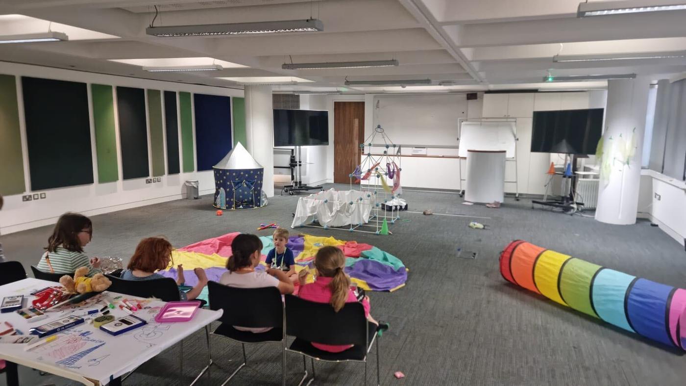 A meeting room set up as a crèche with a parachute game, craft table and play tunnel