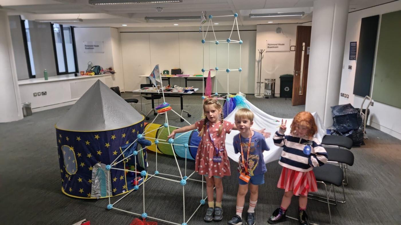 Children in an office meeting room with a rocket tent and den building kit