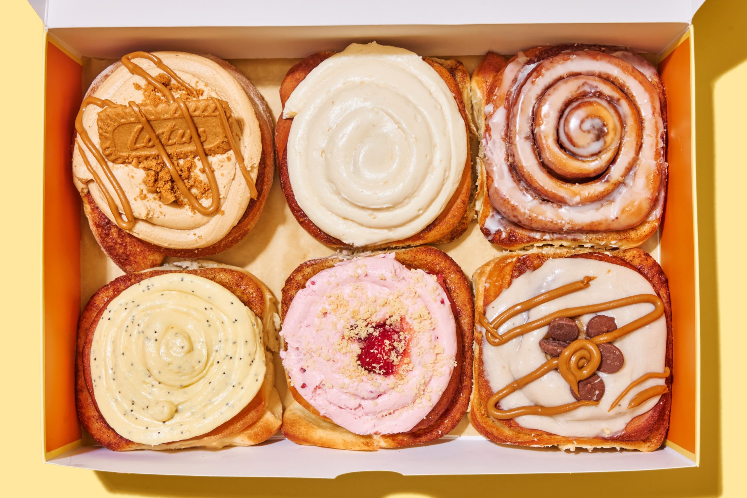 Cream cheese frosting being spread over a Benji's Buns cinnamon roll