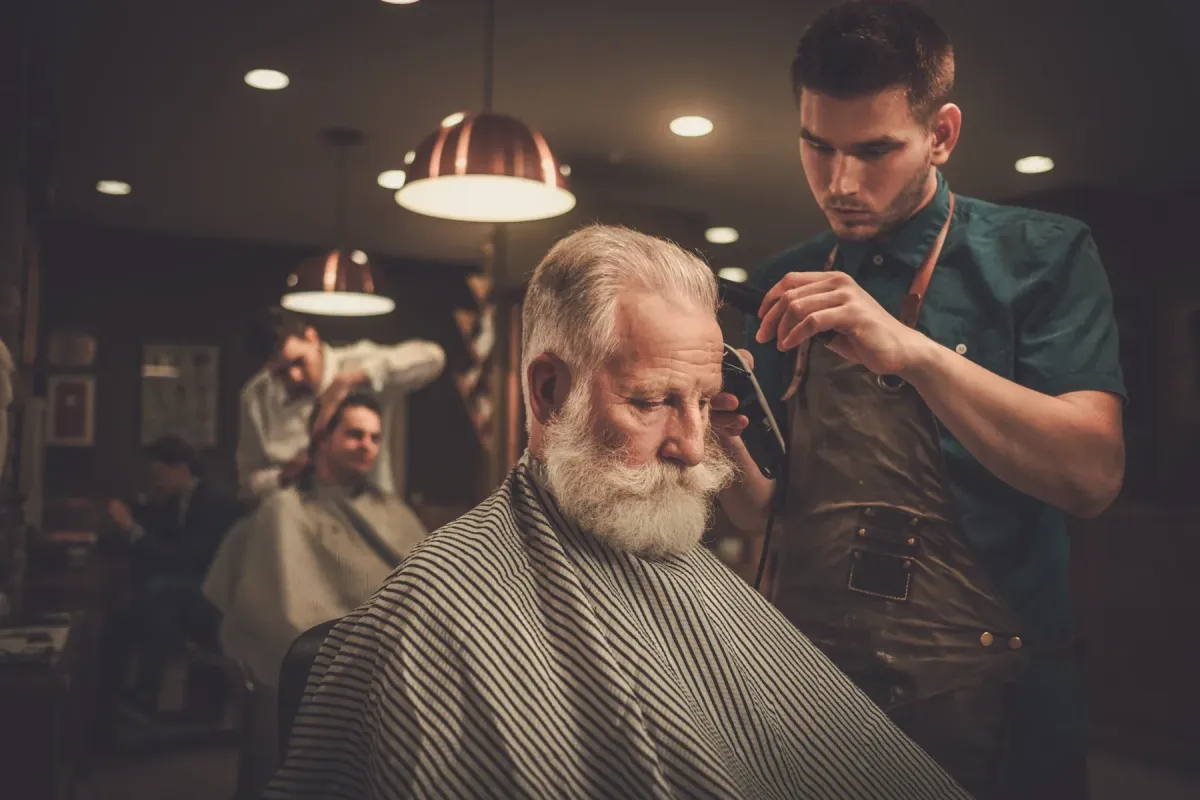 Barber at Scuttlebutt Barbershop in Portsmouth, NH giving a haircut to an older gentleman in a warm, vintage-style barbershop.