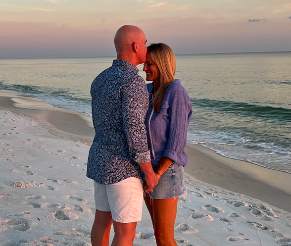 Allan and Nicole Blain stand forehead-to-forehead on a serene beach at sunset, holding hands and smiling — symbolizing unity, love, and high-performance partnership.