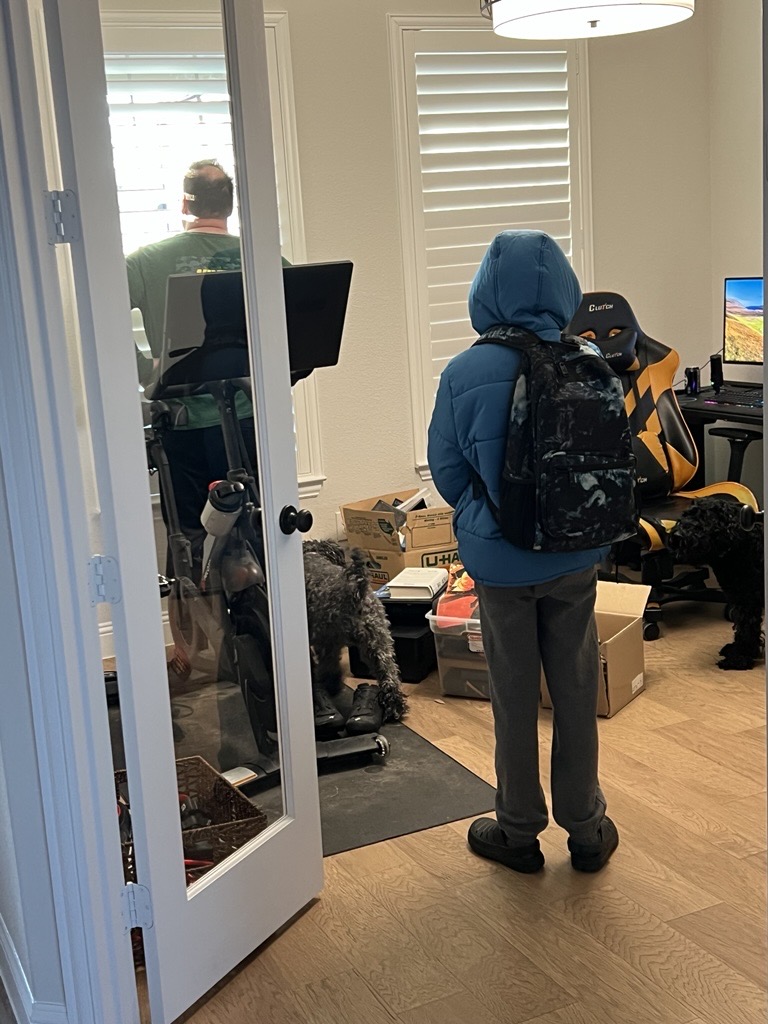 A boy standing in a doorway looking at his father who is staring out of a window