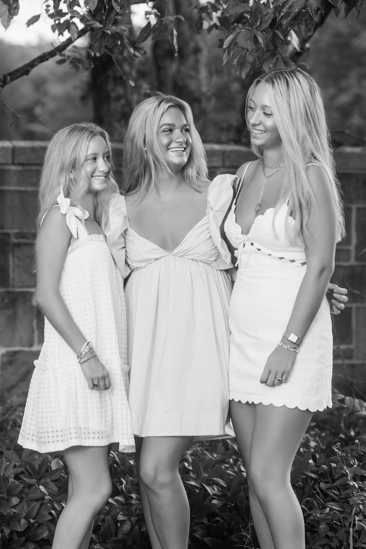 Three sisters stand close together, giggling and leaning into each other, sharing an easy, joyful moment that feels like home.