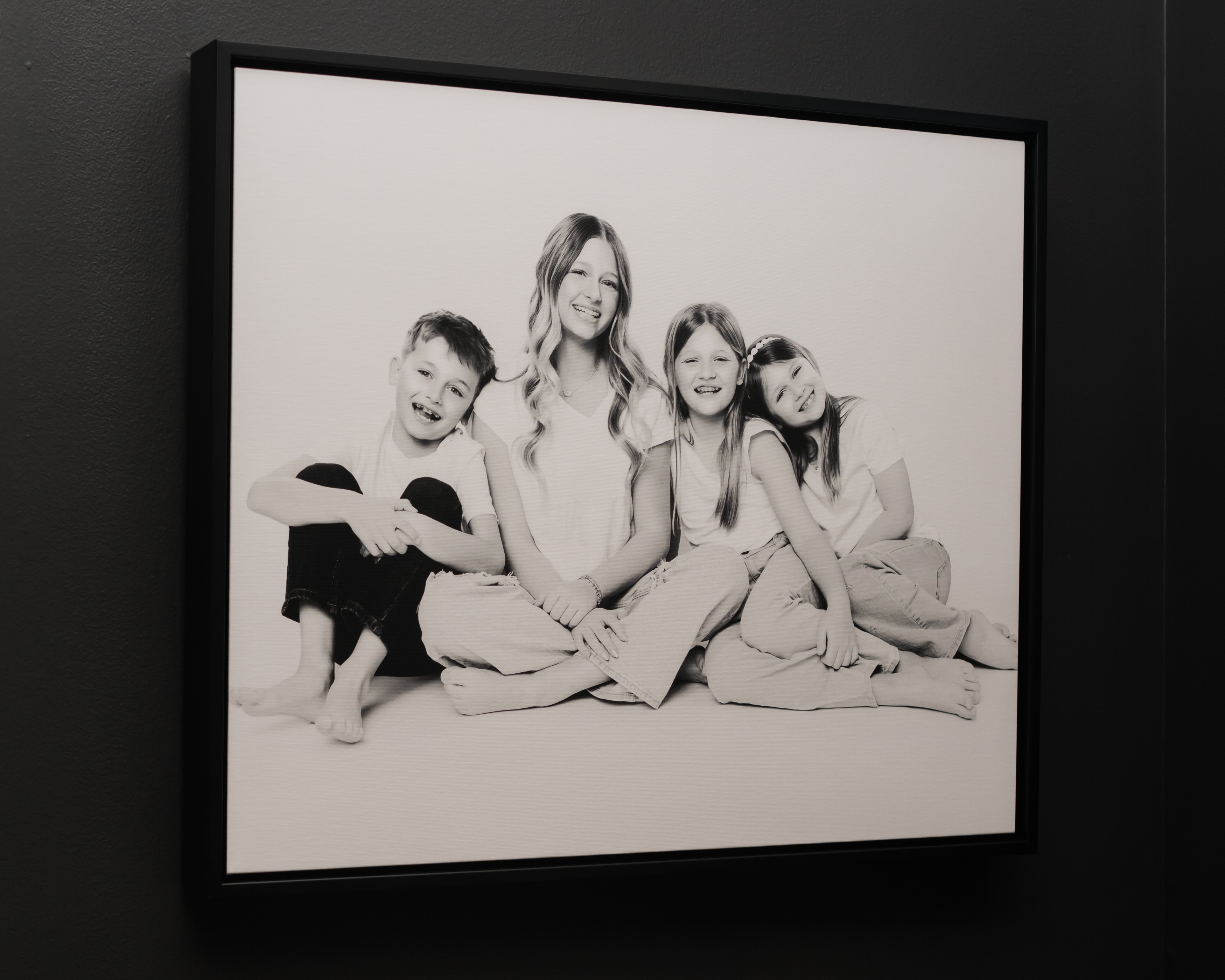 Framed black-and-white family portrait artwork of four siblings sitting closely together and smiling, creating a timeless reminder of their sibling connection on the wall of a Nashville home.